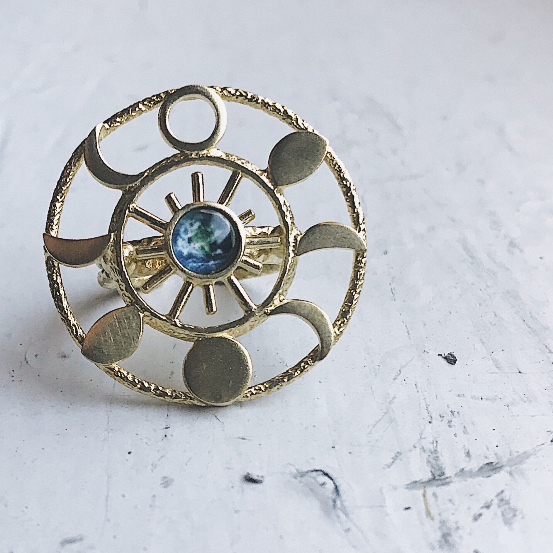 Large Moon Phase Statement Cocktail Ring featuring Earth in glass surrounded by eight moon phases in a textured raw brass gold tone.