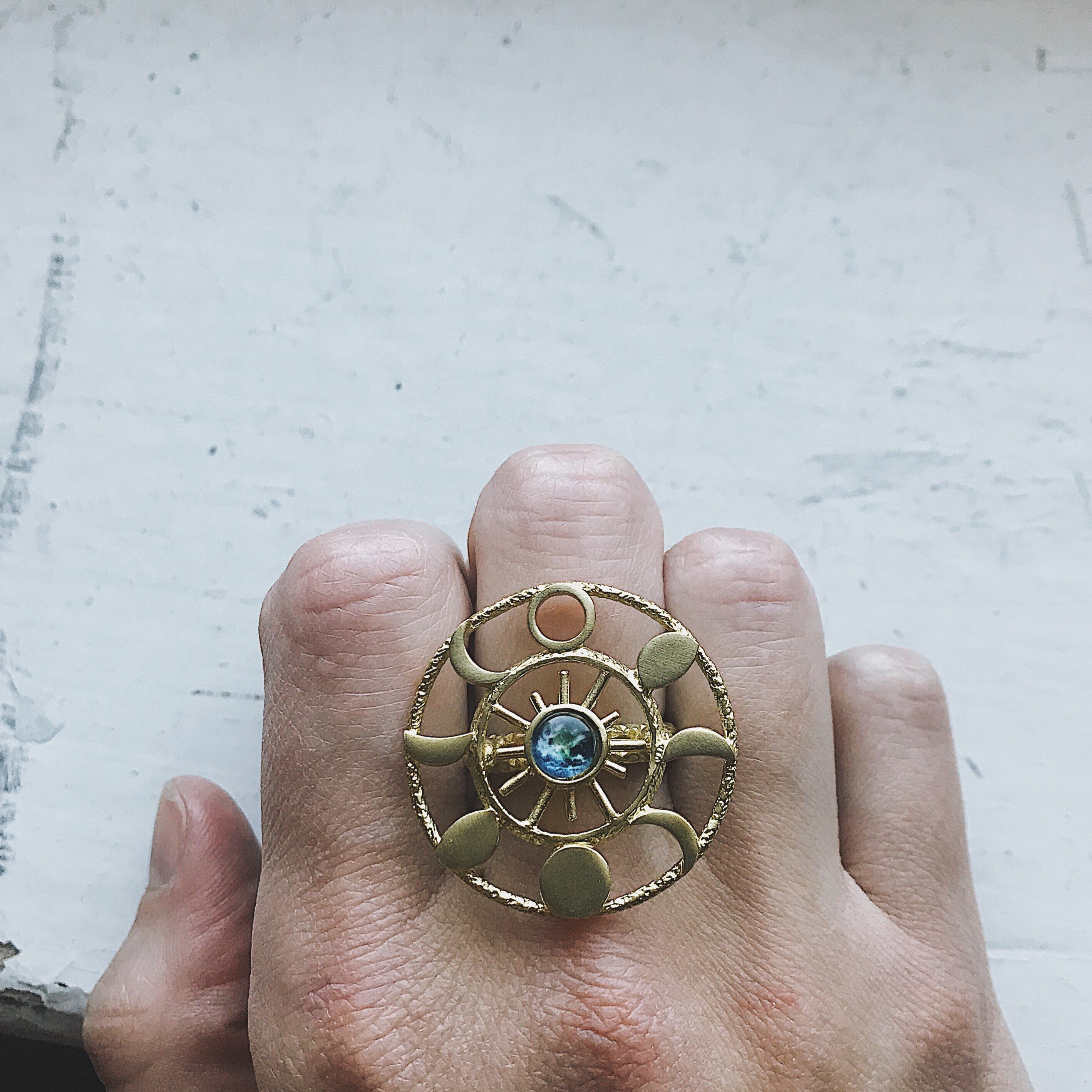 Large Moon Phase Statement Cocktail Ring featuring Earth in glass surrounded by eight moon phases in a textured raw brass gold tone.