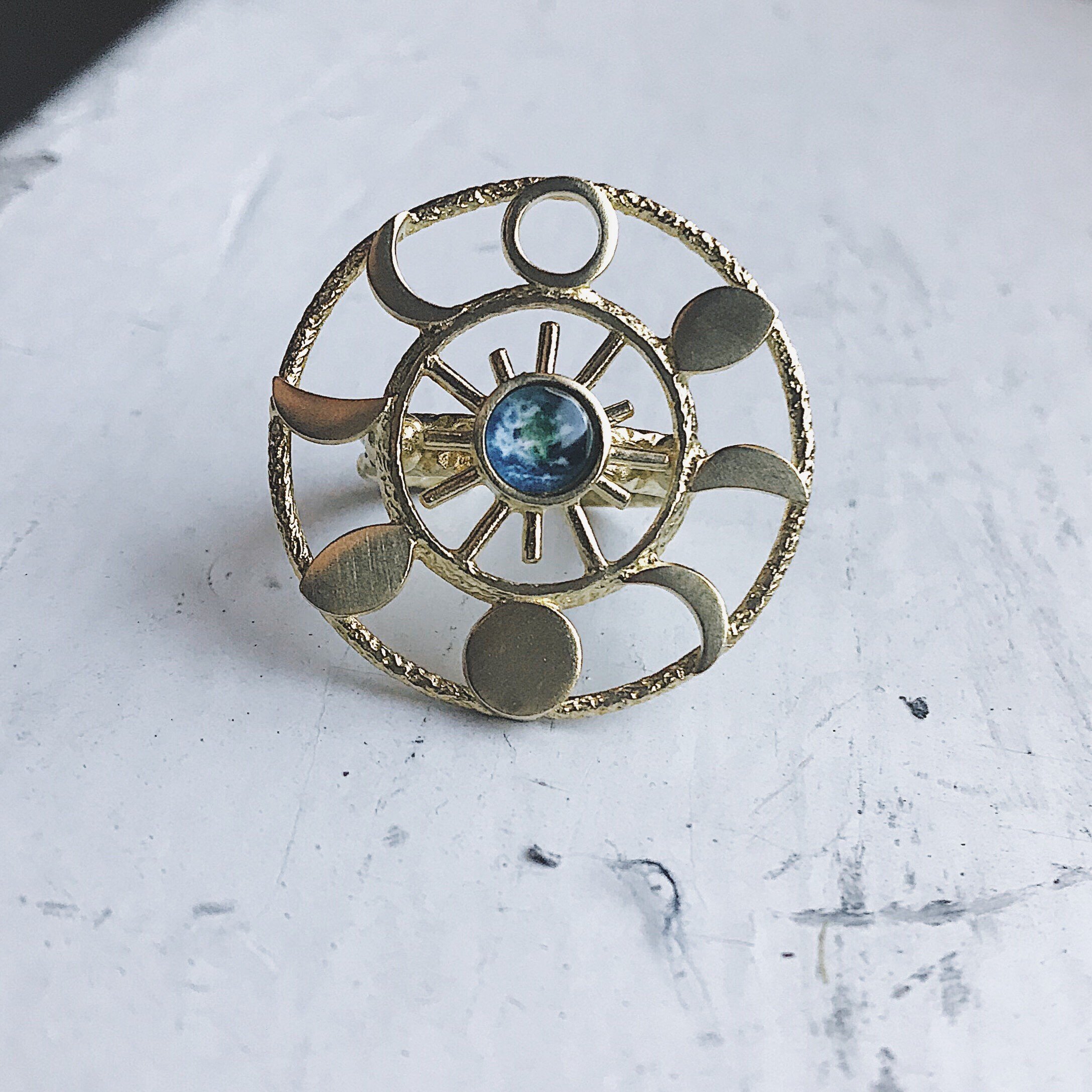 Large Moon Phase Statement Cocktail Ring featuring Earth in glass surrounded by eight moon phases in a textured raw brass gold tone.