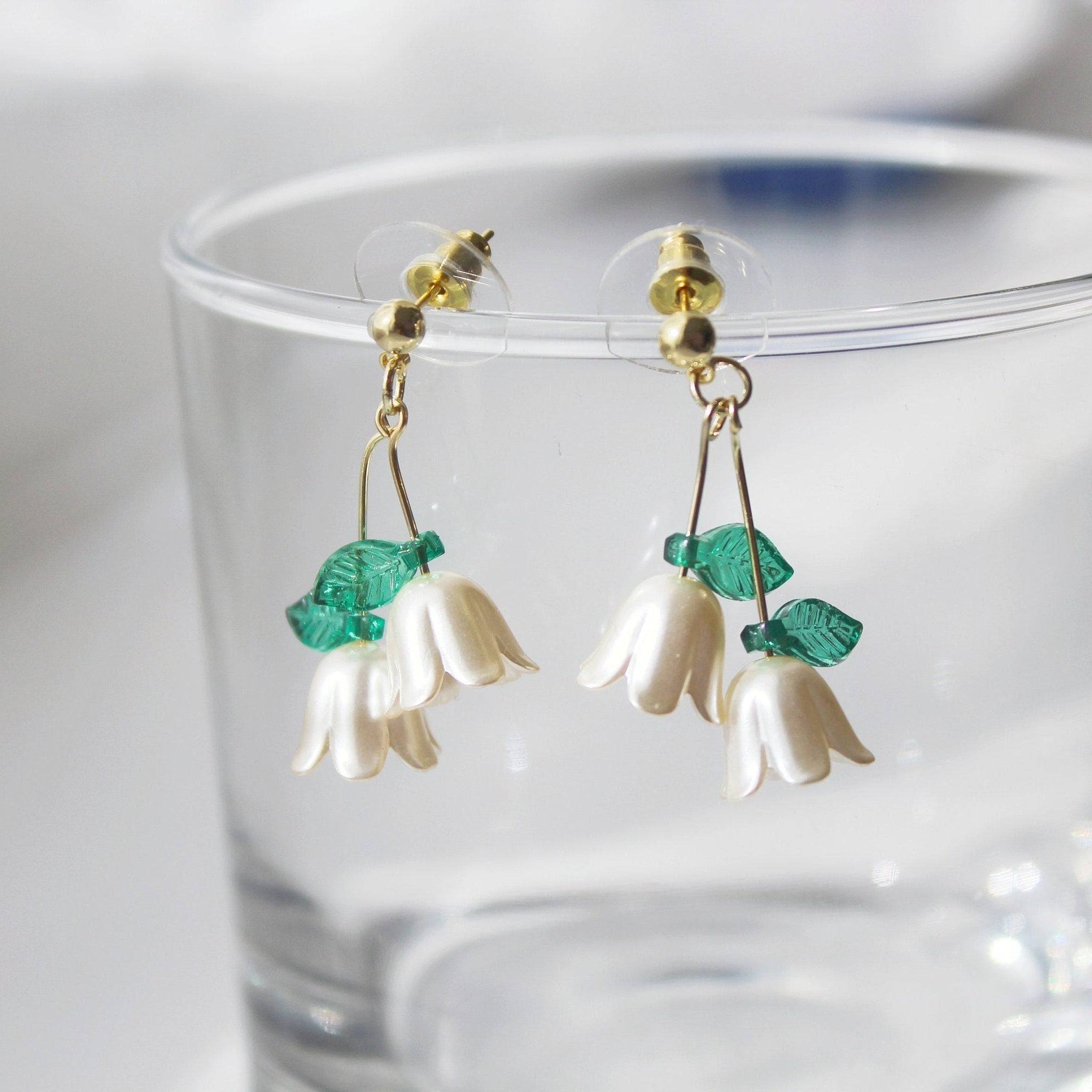 Elegant Lily of the Valley drop earrings featuring white flowers and green leaves, crafted with sterling silver and bronze.