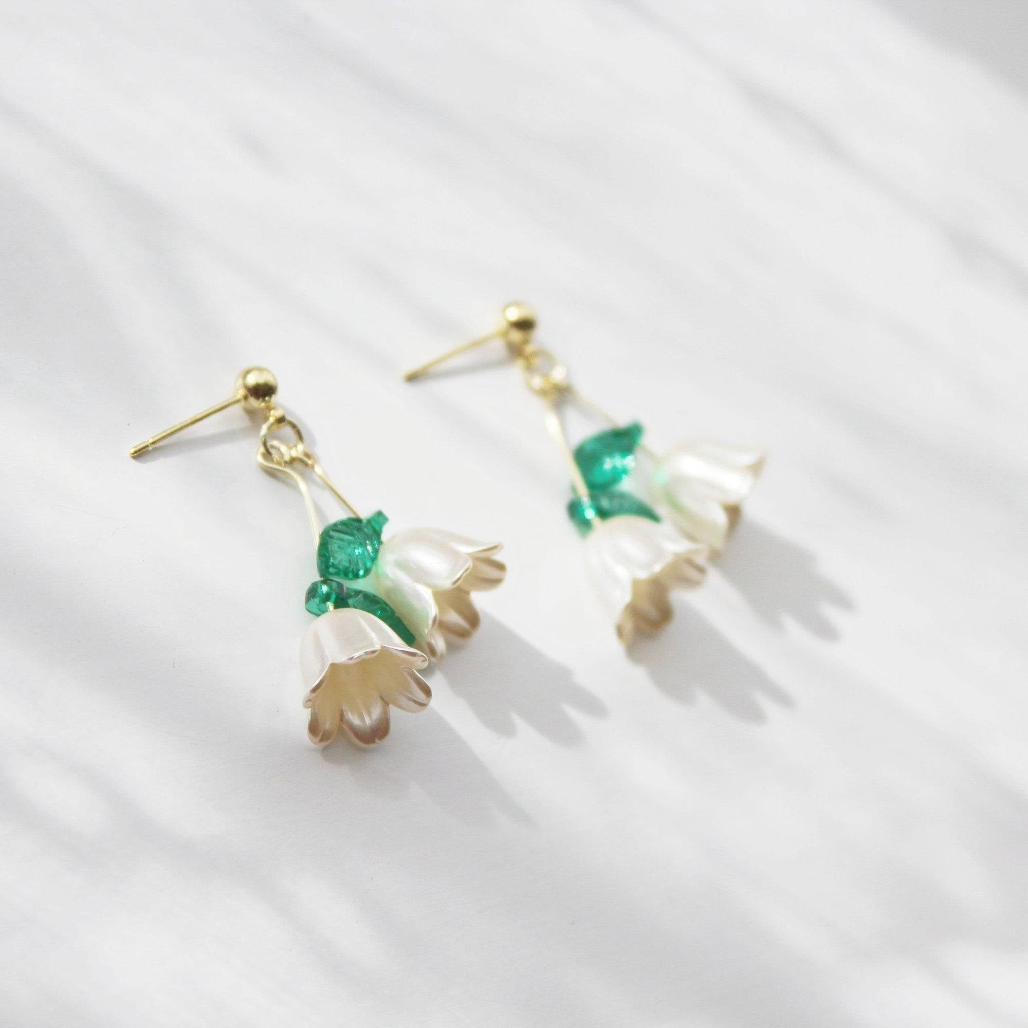 Elegant Lily of the Valley drop earrings featuring white flowers and green leaves, crafted with sterling silver and bronze.