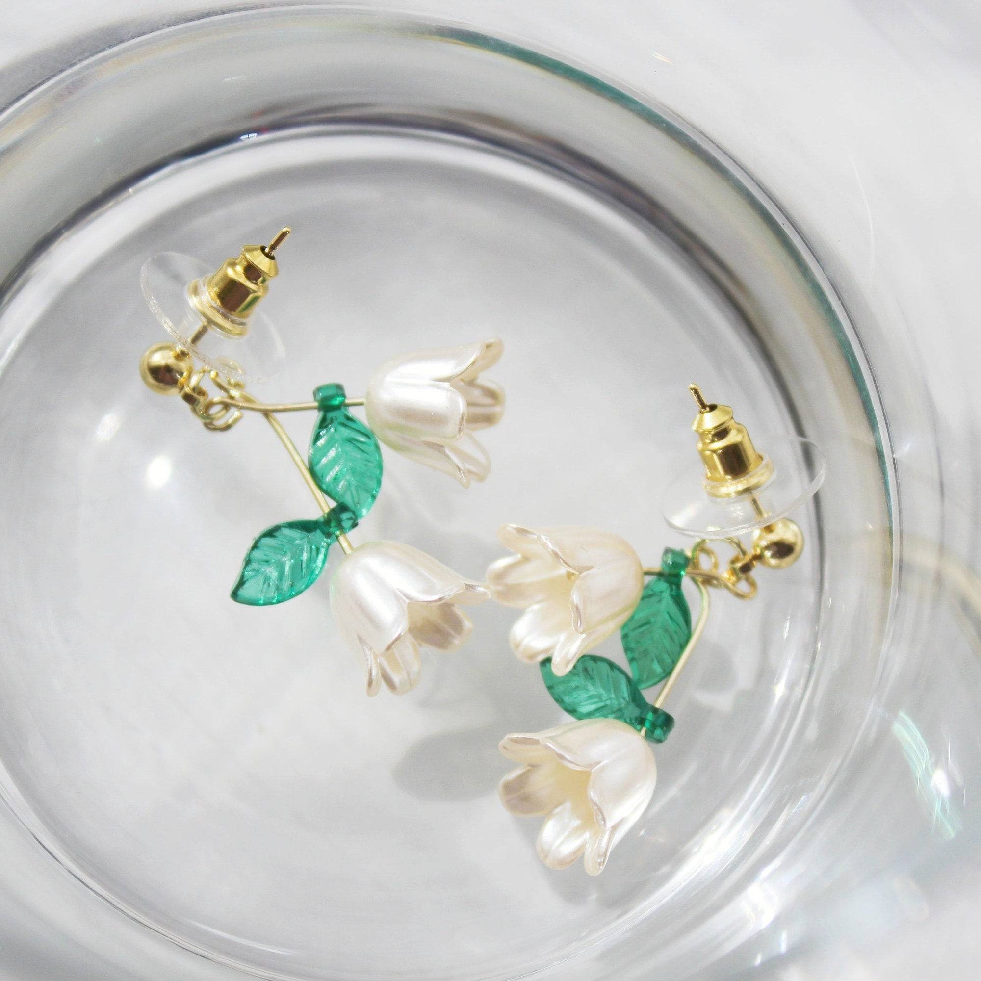 Elegant Lily of the Valley drop earrings featuring white flowers and green leaves, crafted with sterling silver and bronze.