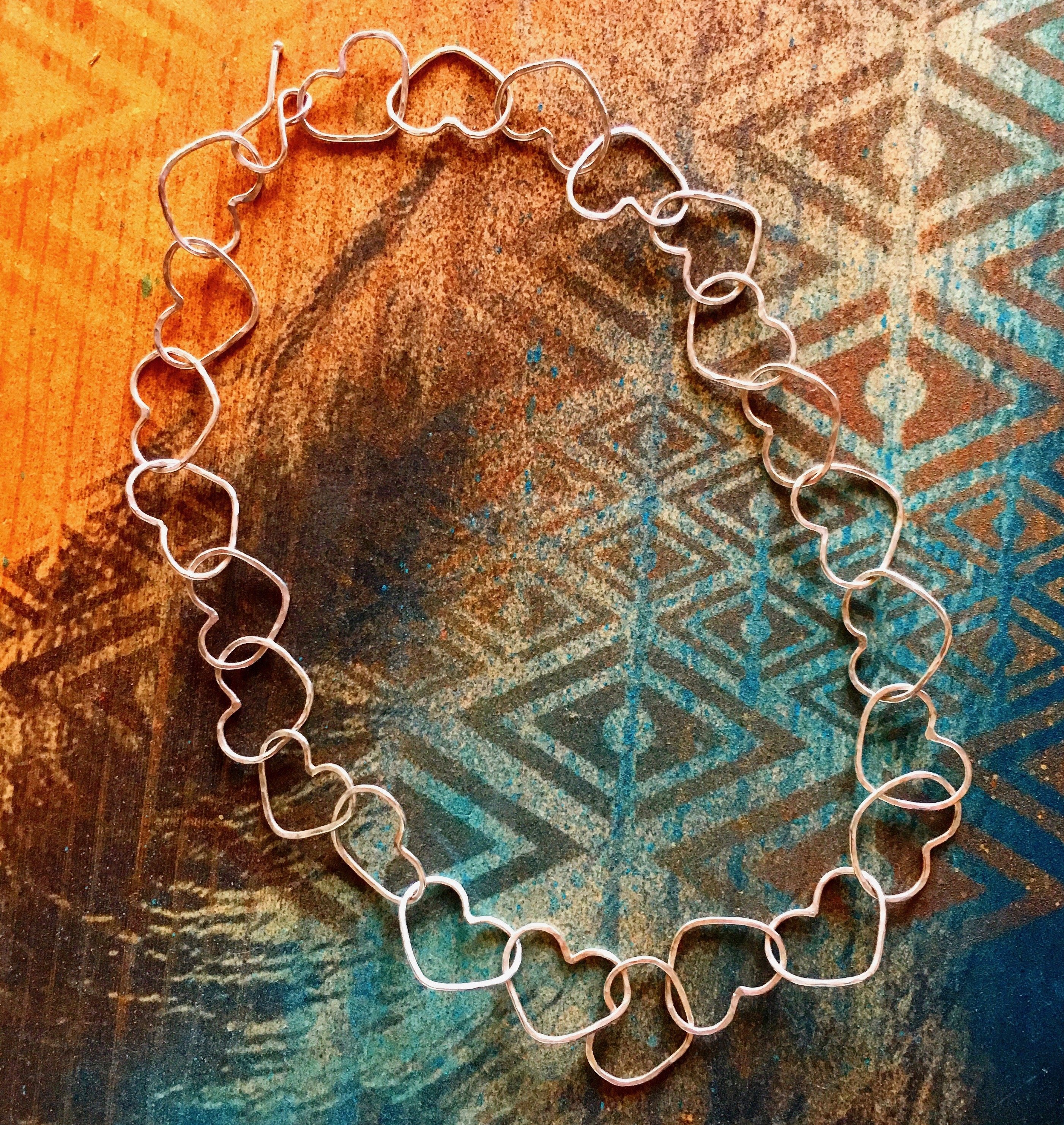 A handmade Linked Heart Chakra Necklace featuring 22 unique heart links, crafted from 14-gauge wire with a rustic finish.