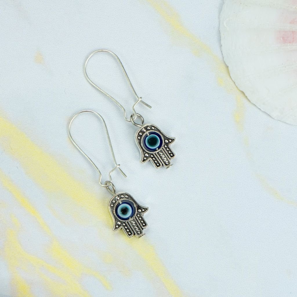 Long silver evil eye hamsa earrings featuring intricate designs and a huggie latch back style, perfect for boho fashion.