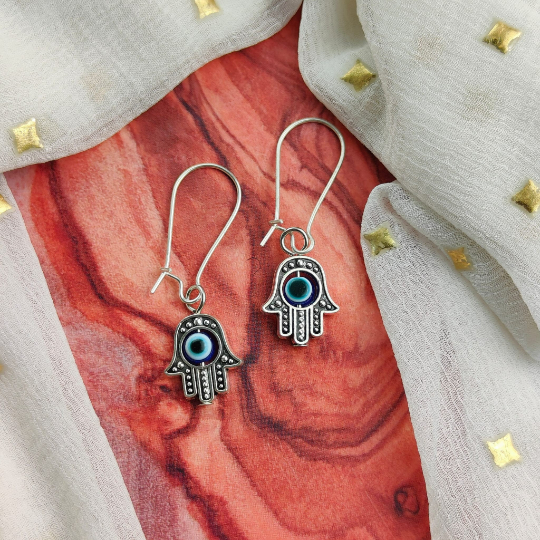 Long silver evil eye hamsa earrings featuring intricate designs and a huggie latch back style, perfect for boho fashion.