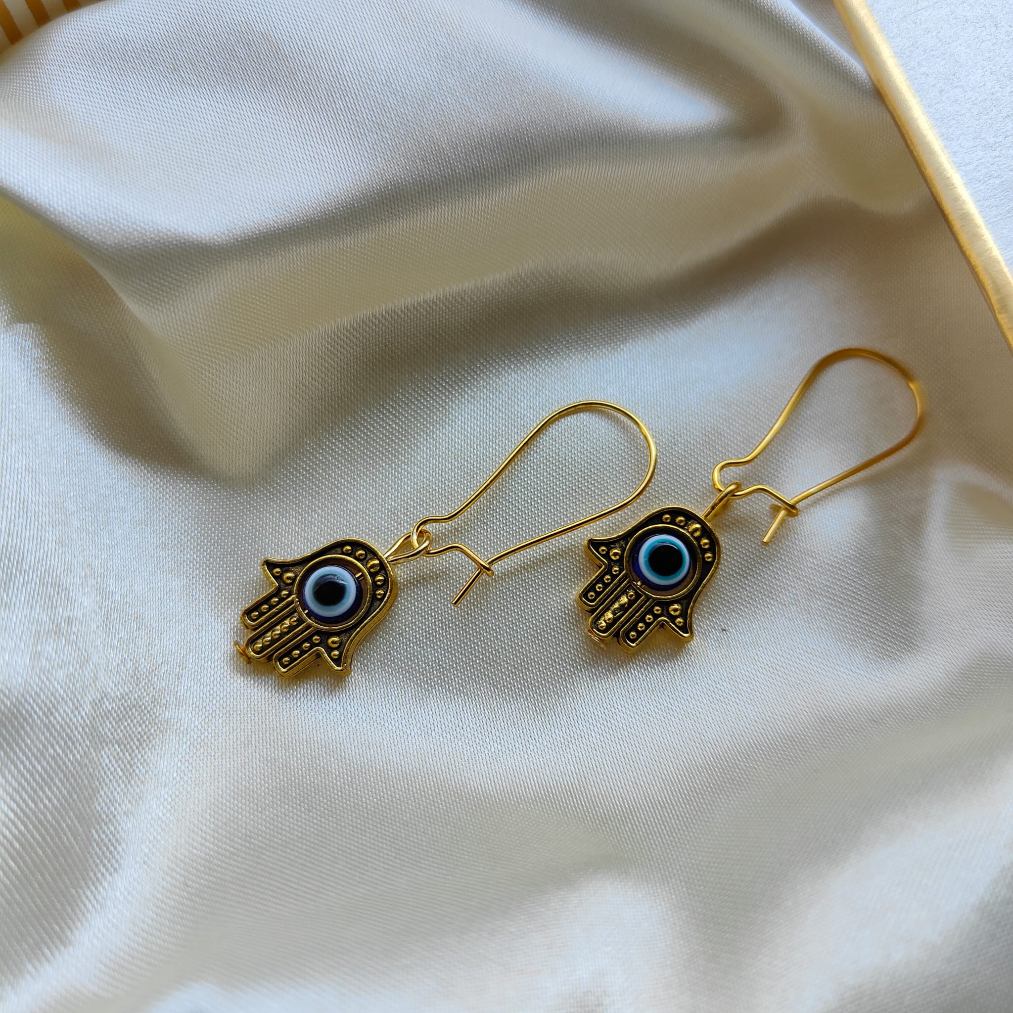 Long silver evil eye hamsa earrings featuring intricate designs and a huggie latch back style, perfect for boho fashion.