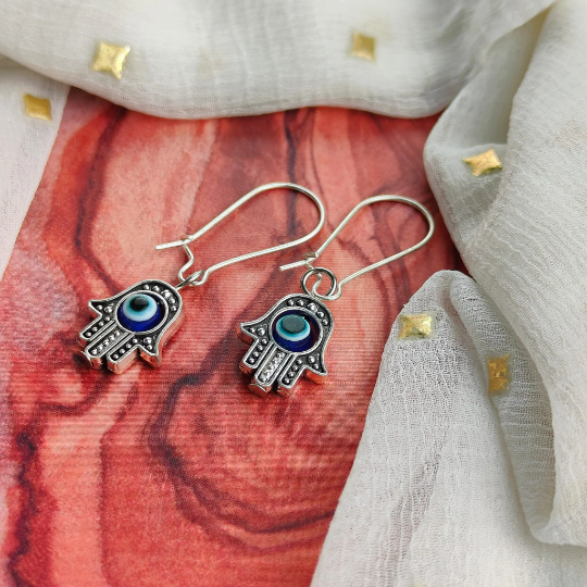 Long silver evil eye hamsa earrings featuring intricate designs and a huggie latch back style, perfect for boho fashion.