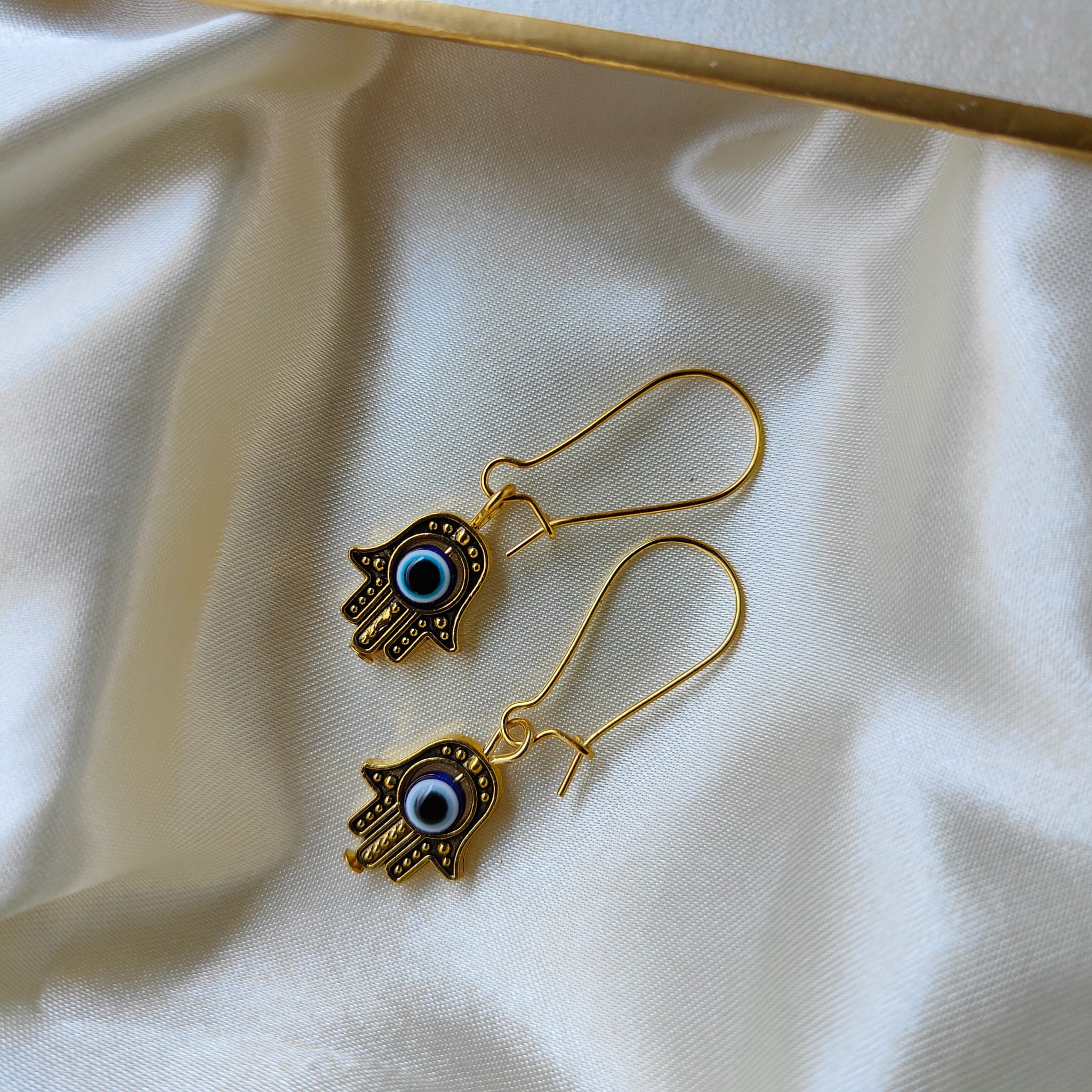 Long silver evil eye hamsa earrings featuring intricate designs and a huggie latch back style, perfect for boho fashion.