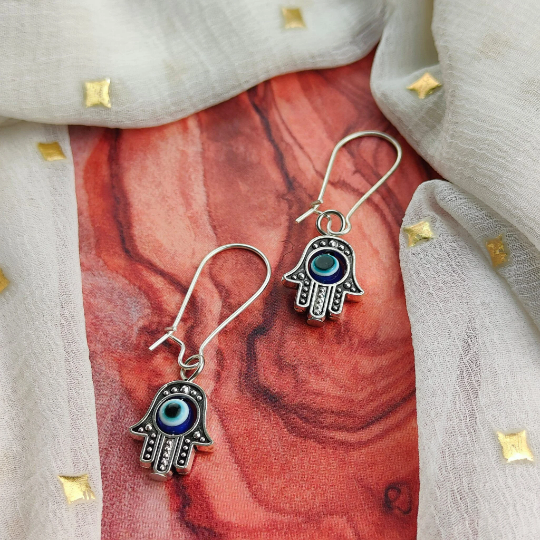 Long silver evil eye hamsa earrings featuring intricate designs and a huggie latch back style, perfect for boho fashion.