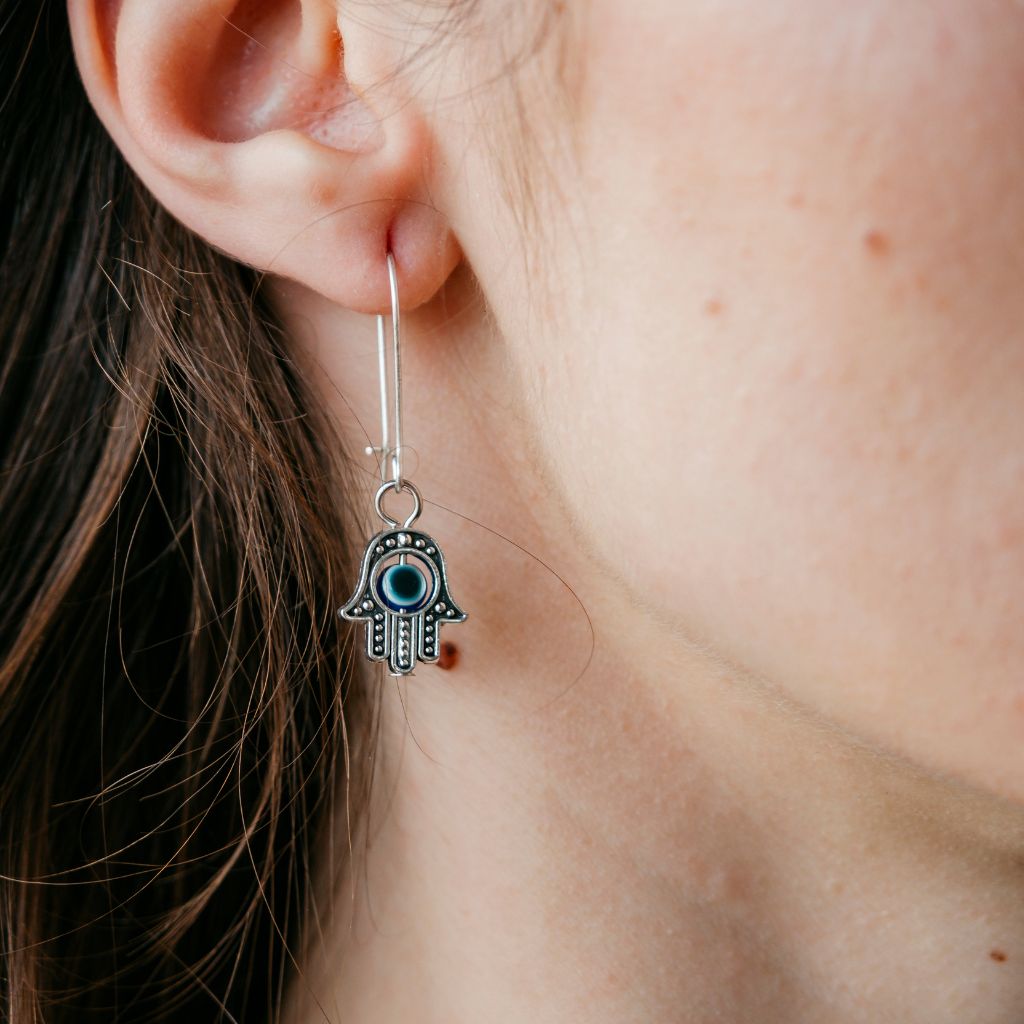 Long silver evil eye hamsa earrings featuring intricate designs and a huggie latch back style, perfect for boho fashion.