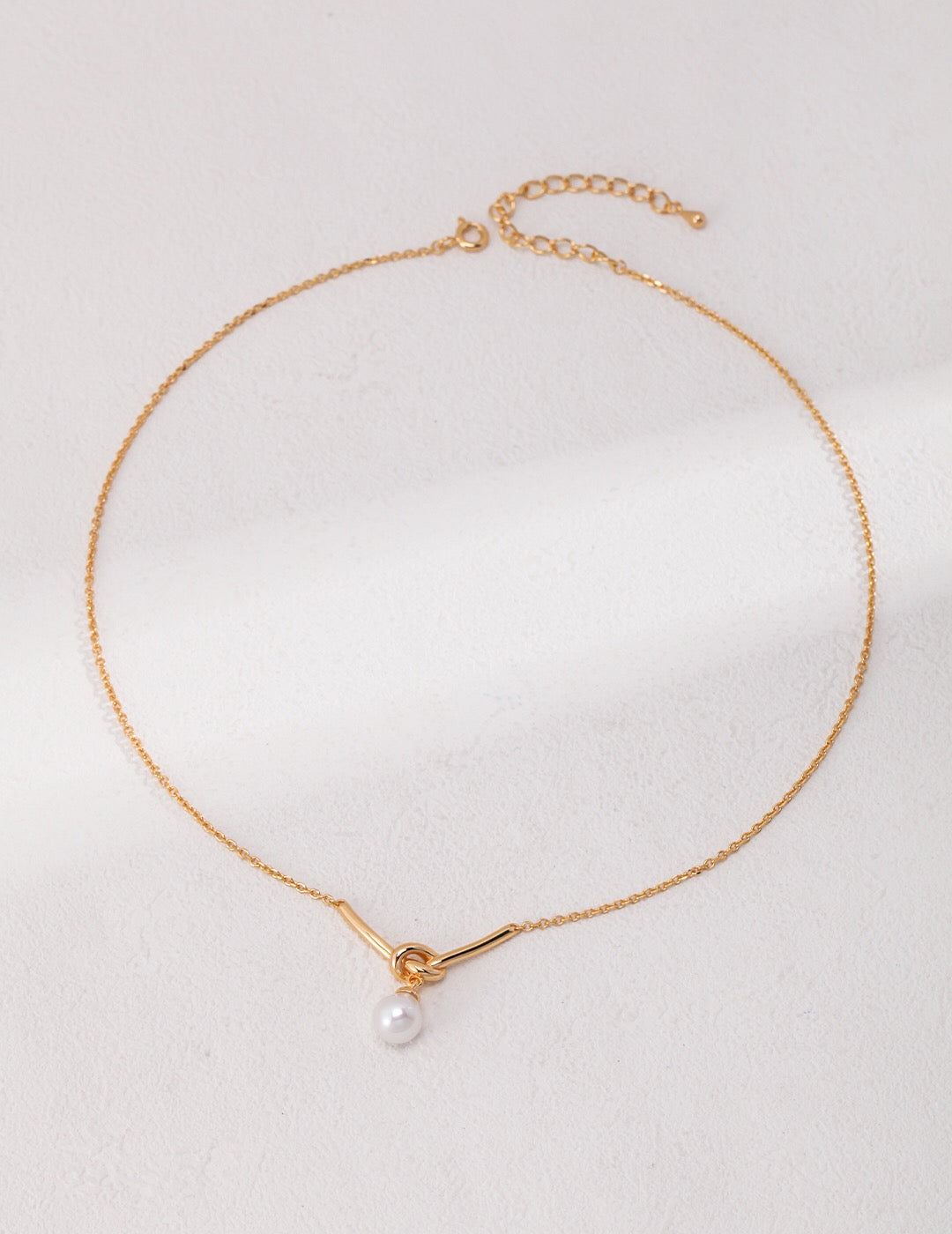 Elegant Love Knot Drop Pearl Necklace featuring natural pearls and gold vermeil, displayed on a soft fabric background.