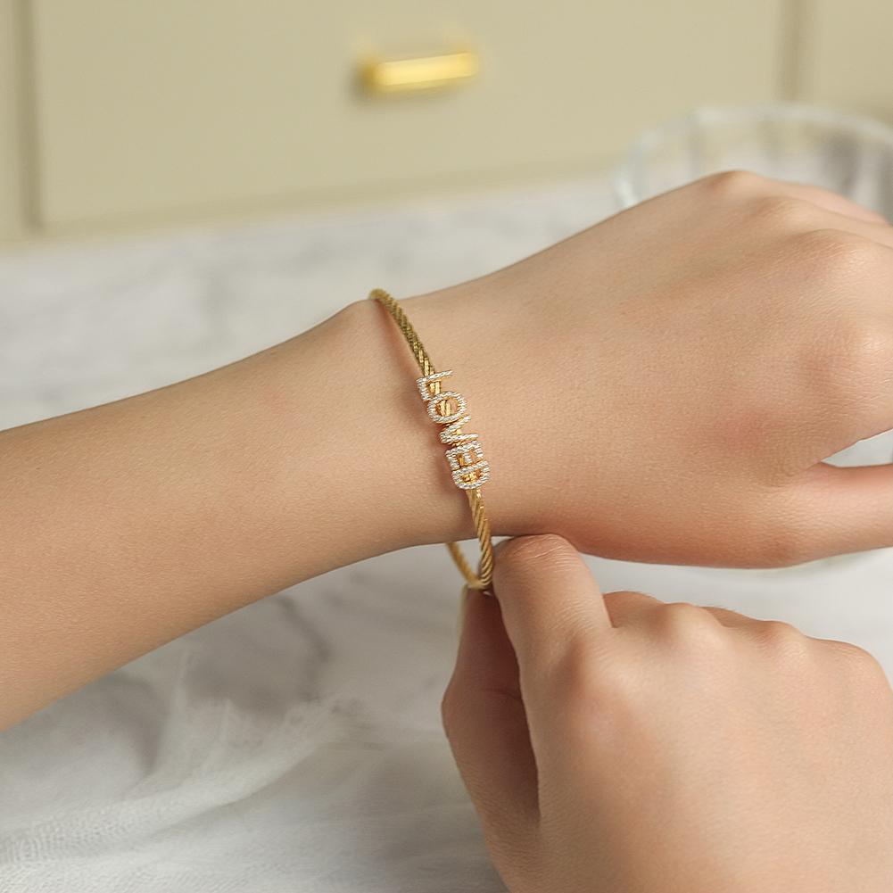 A beautiful 'LOVED' Pavé Bangle Bracelet made of surgical stainless steel with 14K gold plating, featuring a sparkling pavé design.