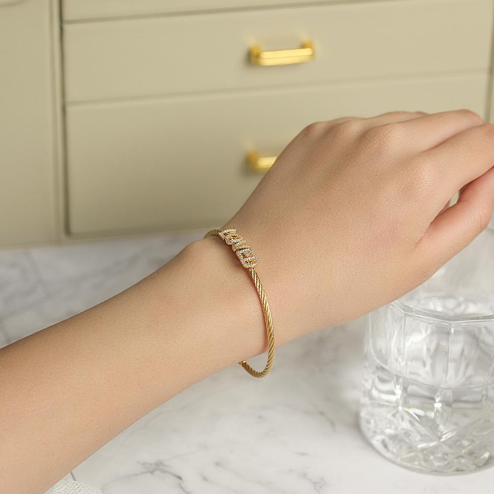 A beautiful 'LOVED' Pavé Bangle Bracelet made of surgical stainless steel with 14K gold plating, featuring a sparkling pavé design.