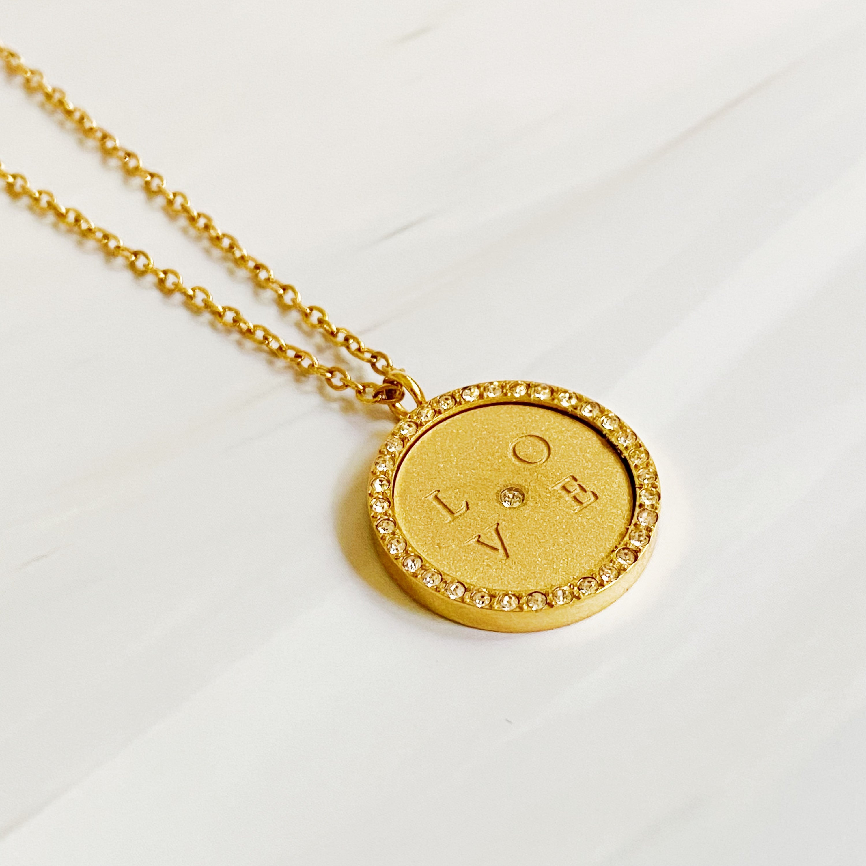 Loveholic Round Pendant Necklace featuring an engraved 'LOVE' design with sparkling cubic zirconia stones on an 18-inch gold plated chain.