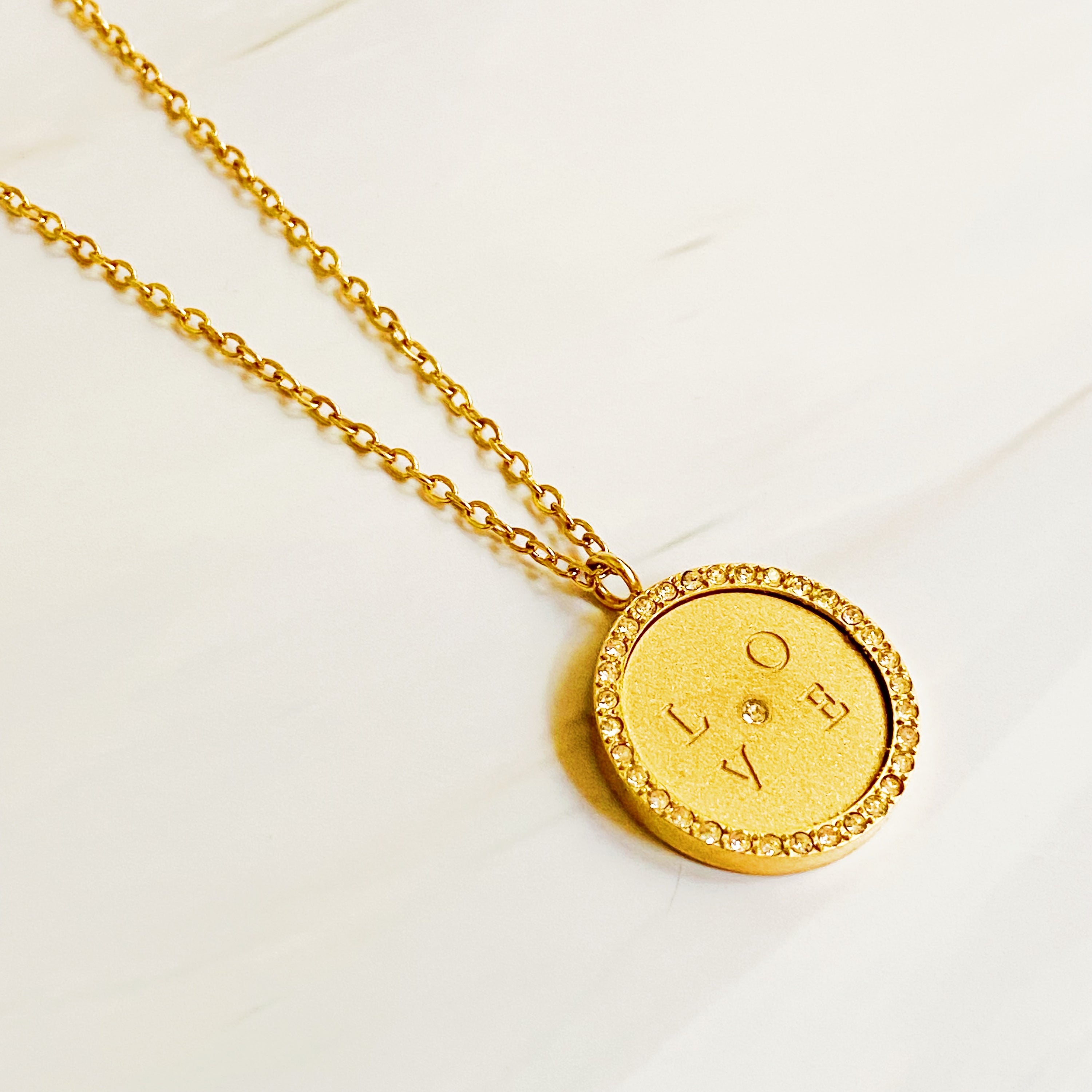 Loveholic Round Pendant Necklace featuring an engraved 'LOVE' design with sparkling cubic zirconia stones on an 18-inch gold plated chain.