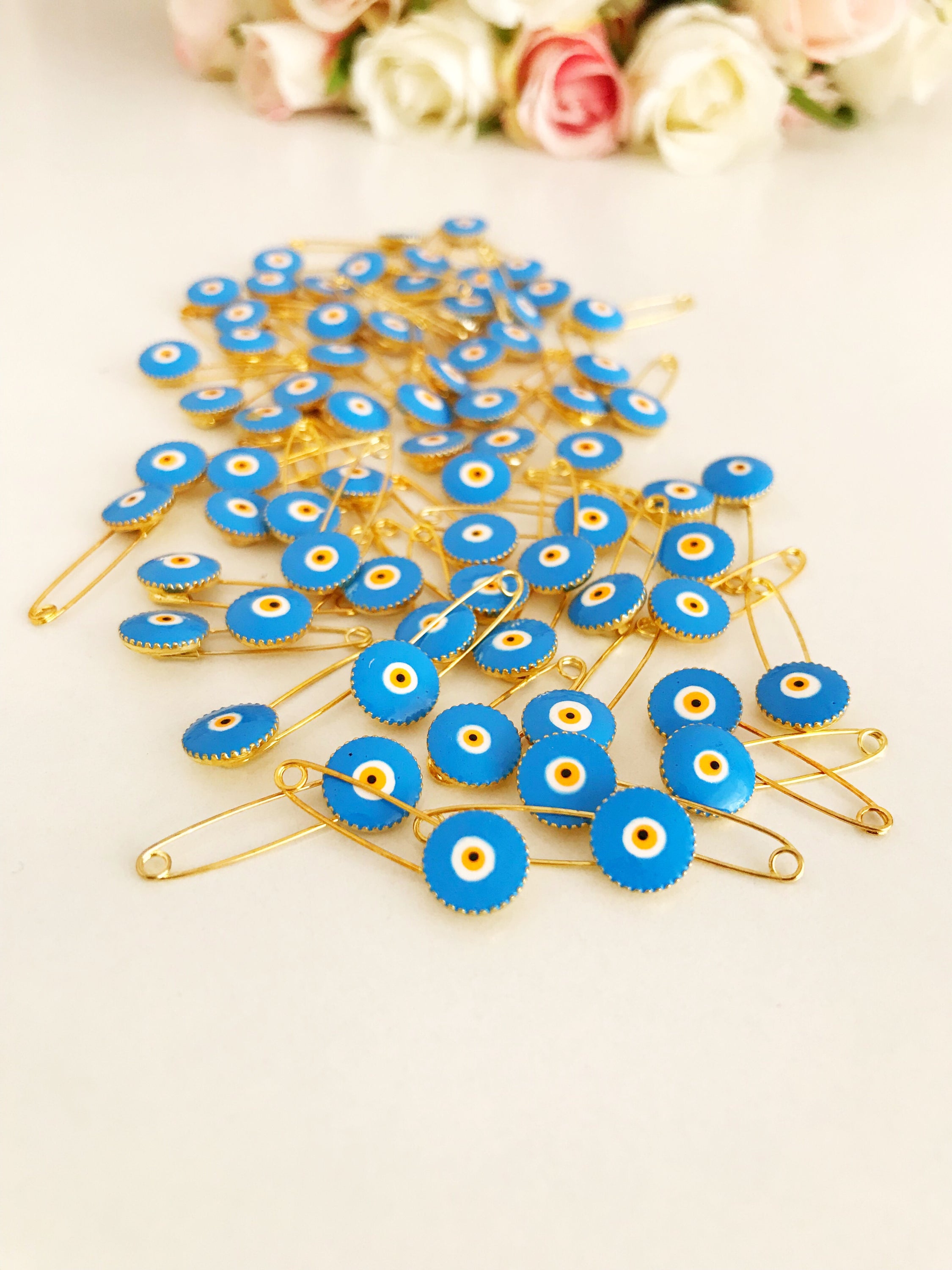 A collection of 50 brass safety pins featuring blue evil eye beads, perfect for weddings and baby showers.