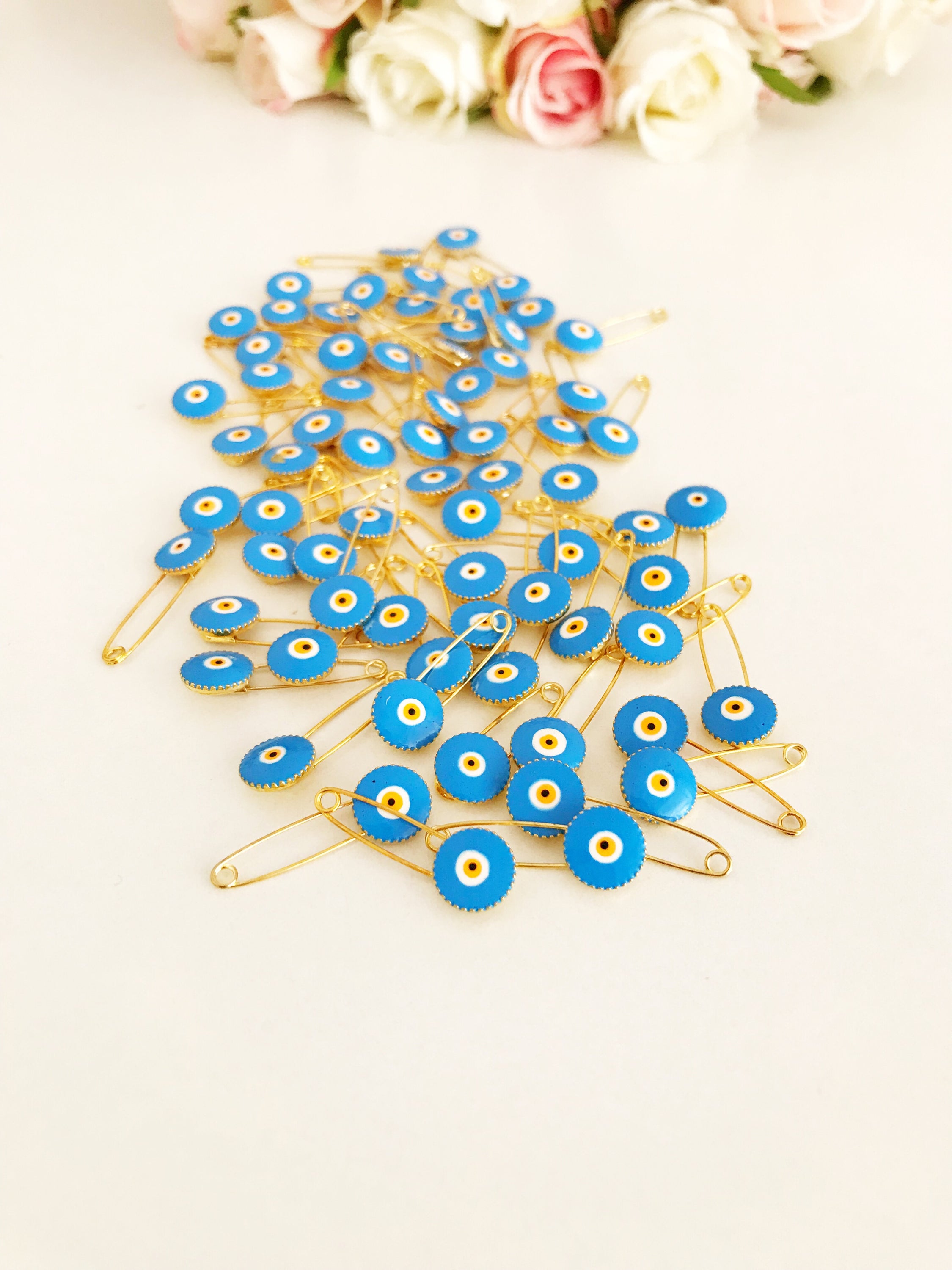 A collection of 50 brass safety pins featuring blue evil eye beads, perfect for weddings and baby showers.