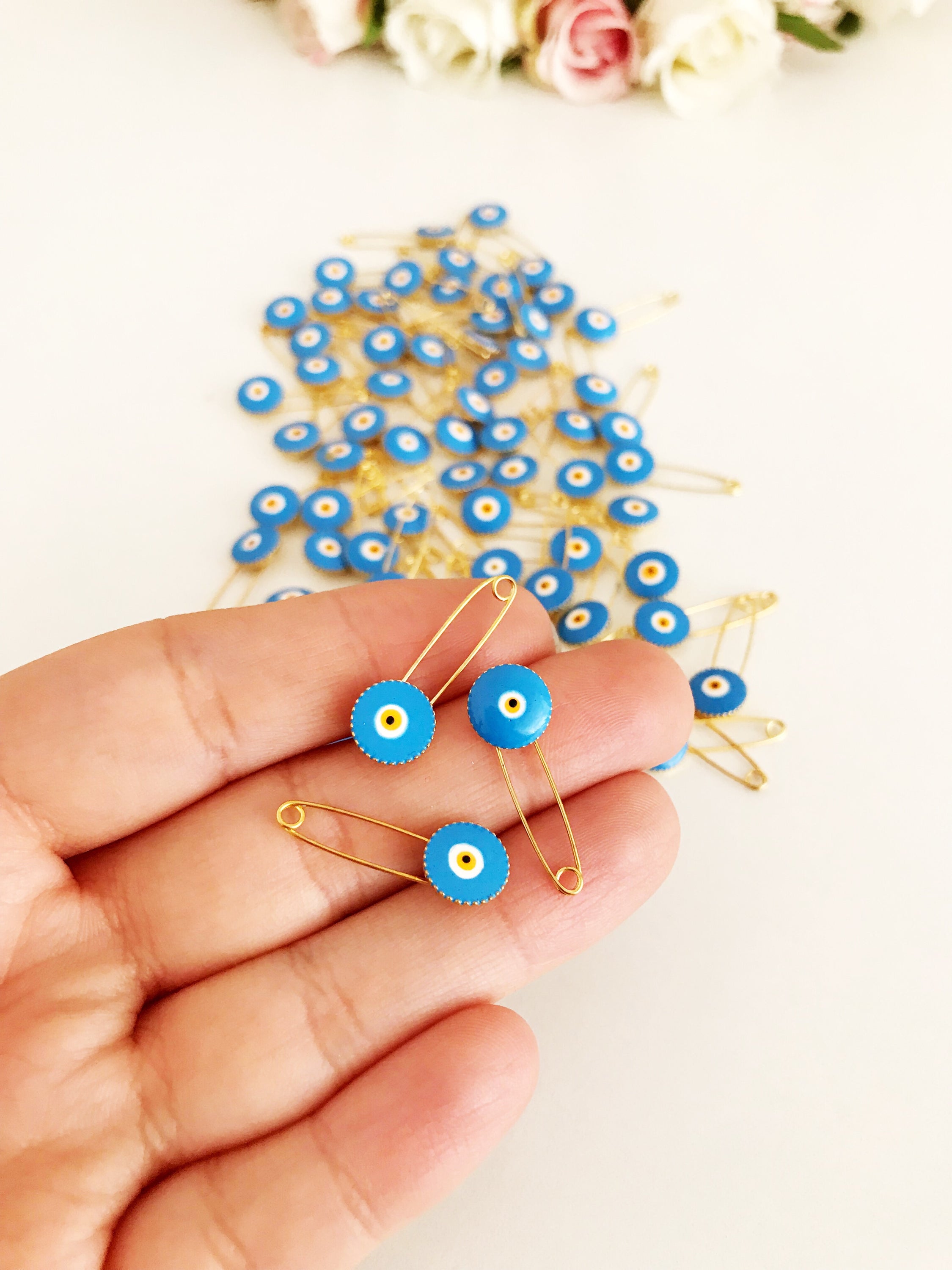 A collection of 50 brass safety pins featuring blue evil eye beads, perfect for weddings and baby showers.