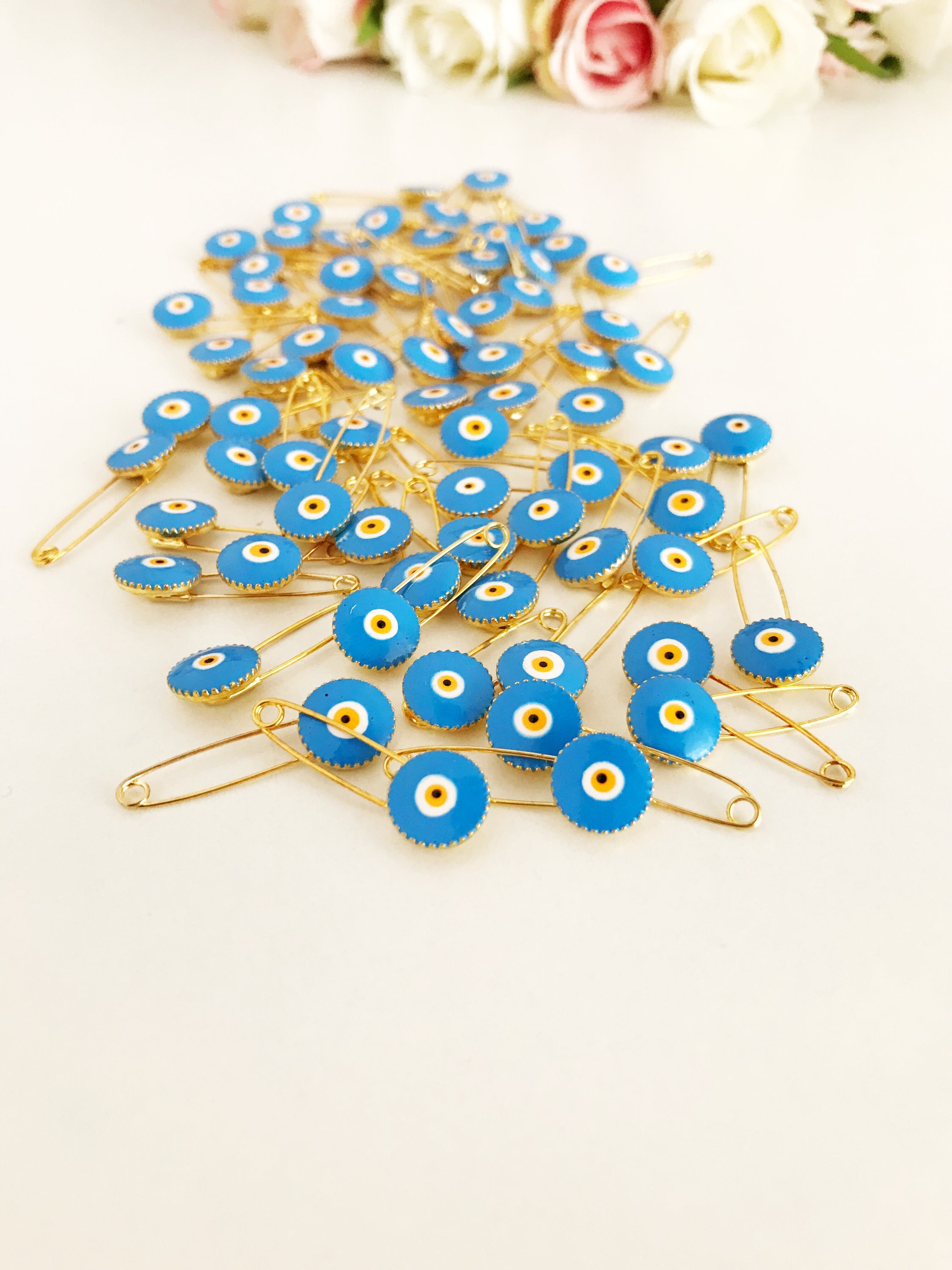 A collection of 50 brass safety pins featuring blue evil eye beads, perfect for weddings and baby showers.