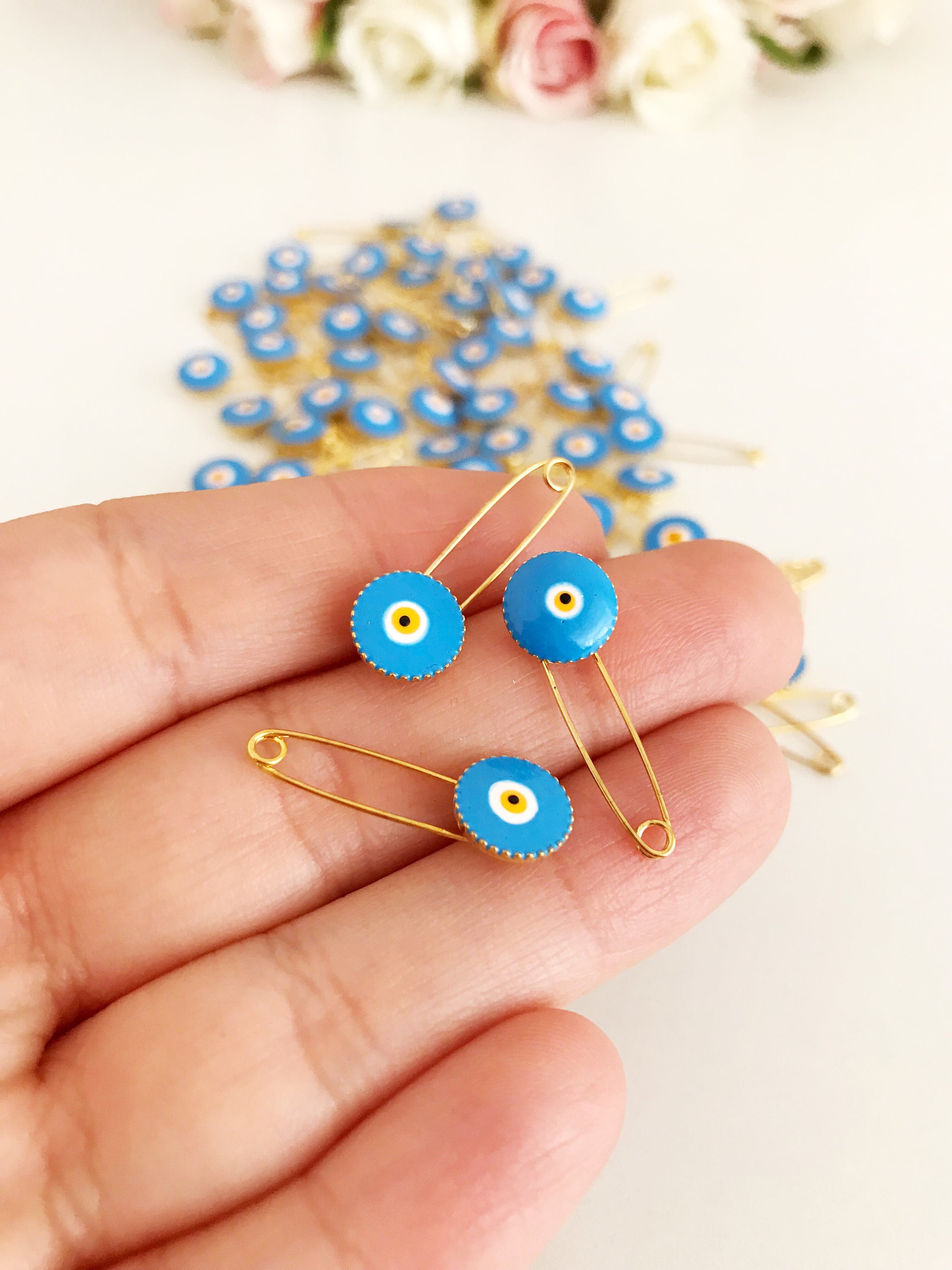 A collection of 50 brass safety pins featuring blue evil eye beads, perfect for weddings and baby showers.