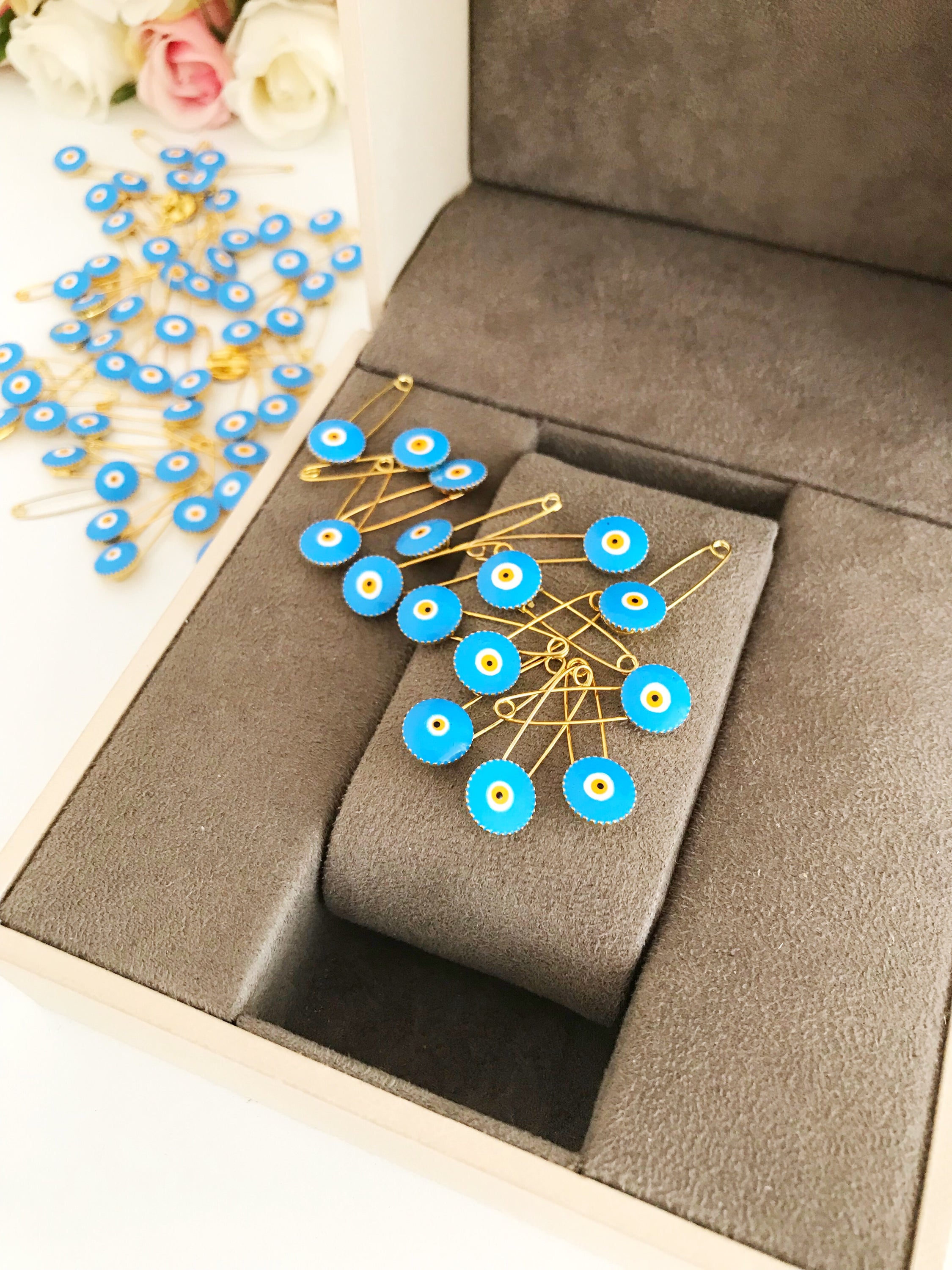 A collection of 50 brass safety pins featuring blue evil eye beads, perfect for weddings and baby showers.