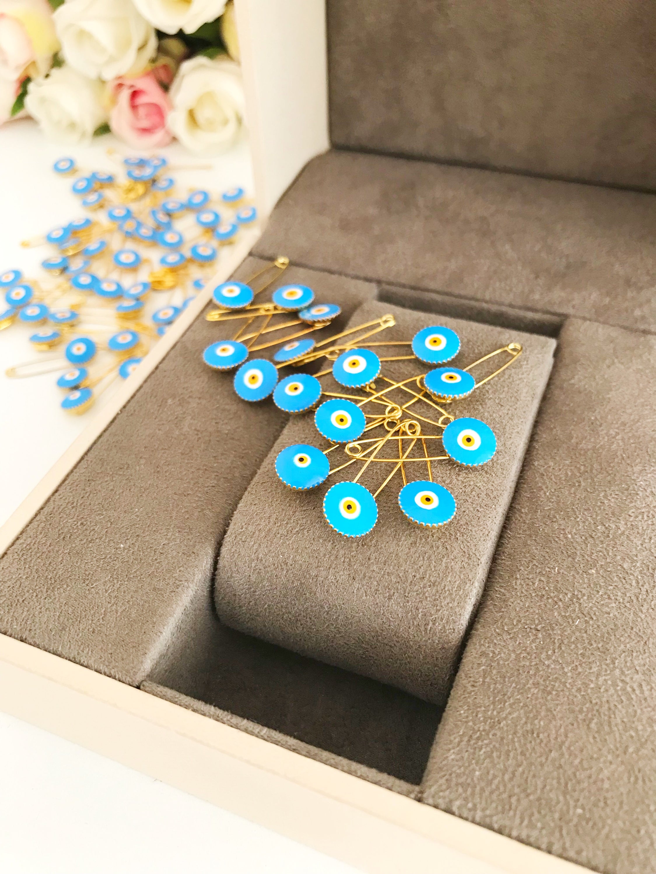 A collection of 50 brass safety pins featuring blue evil eye beads, perfect for weddings and baby showers.