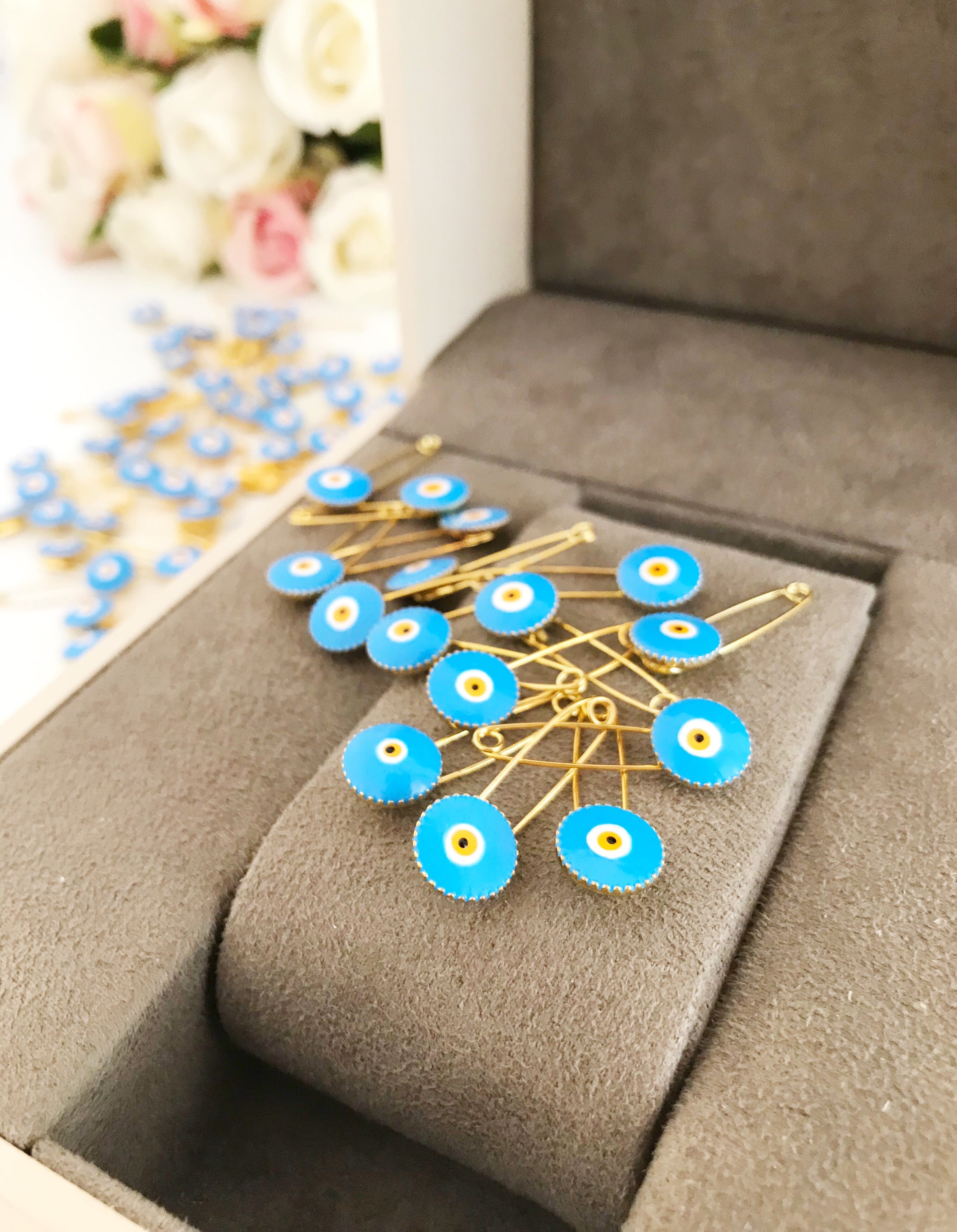 A collection of 50 brass safety pins featuring blue evil eye beads, perfect for weddings and baby showers.