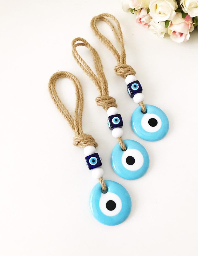 Handmade macrame wall hanging featuring a turquoise glass evil eye bead and blue plastic beads, measuring 21cm in length.