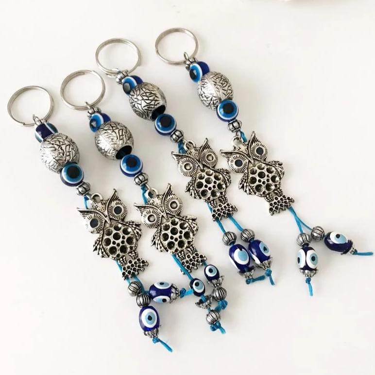 A detailed metal owl keychain featuring a blue evil eye bead, symbolizing protection and luck.