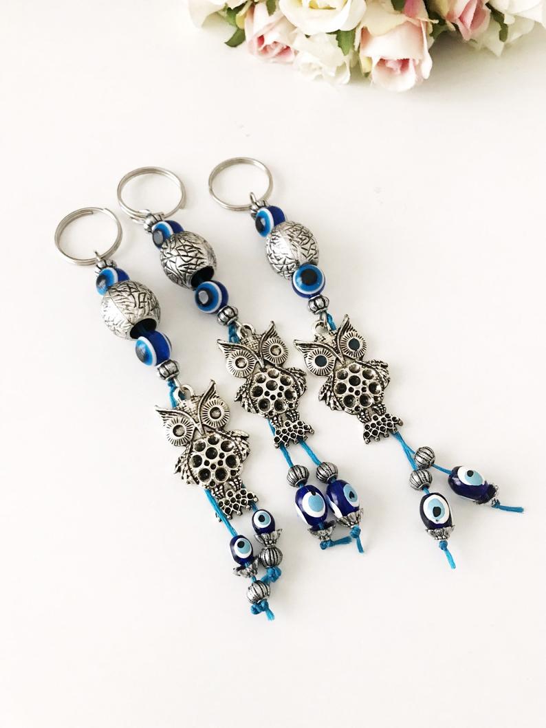 A detailed metal owl keychain featuring a blue evil eye bead, symbolizing protection and luck.