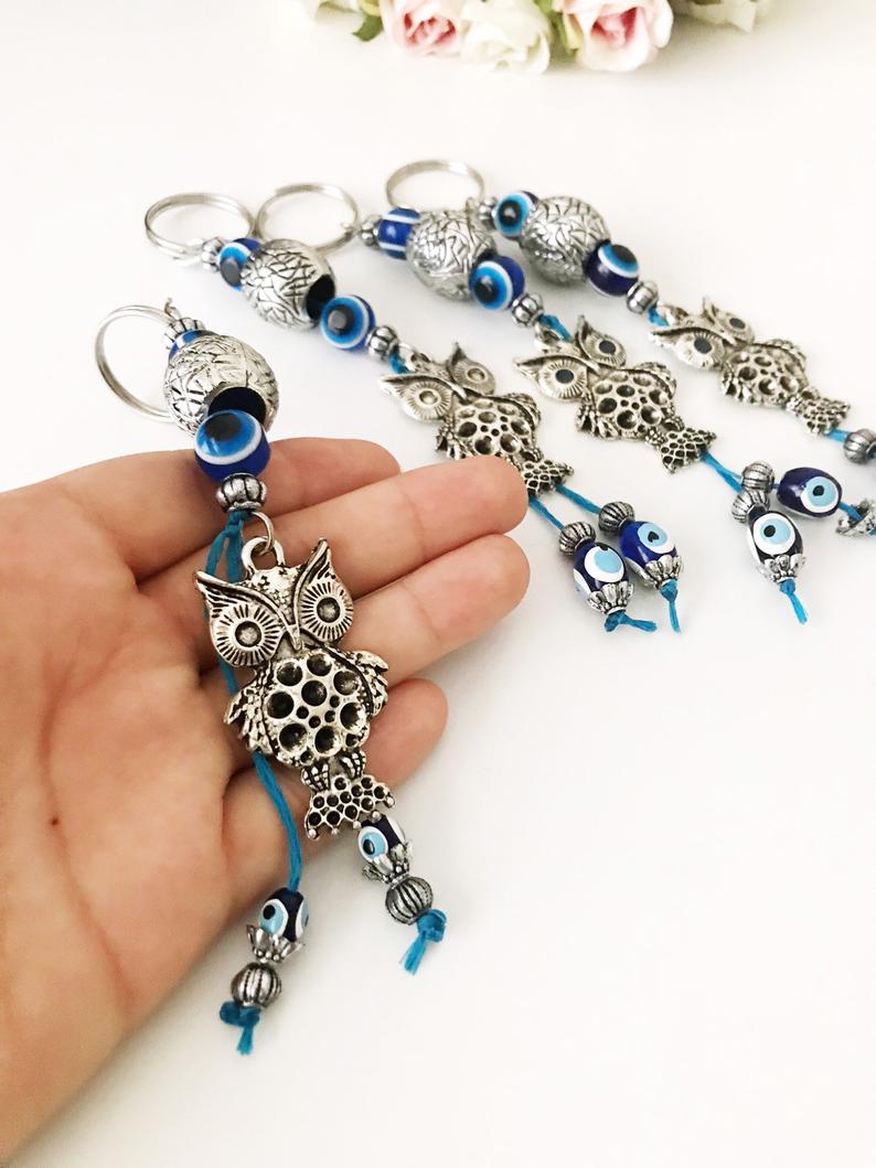 A detailed metal owl keychain featuring a blue evil eye bead, symbolizing protection and luck.