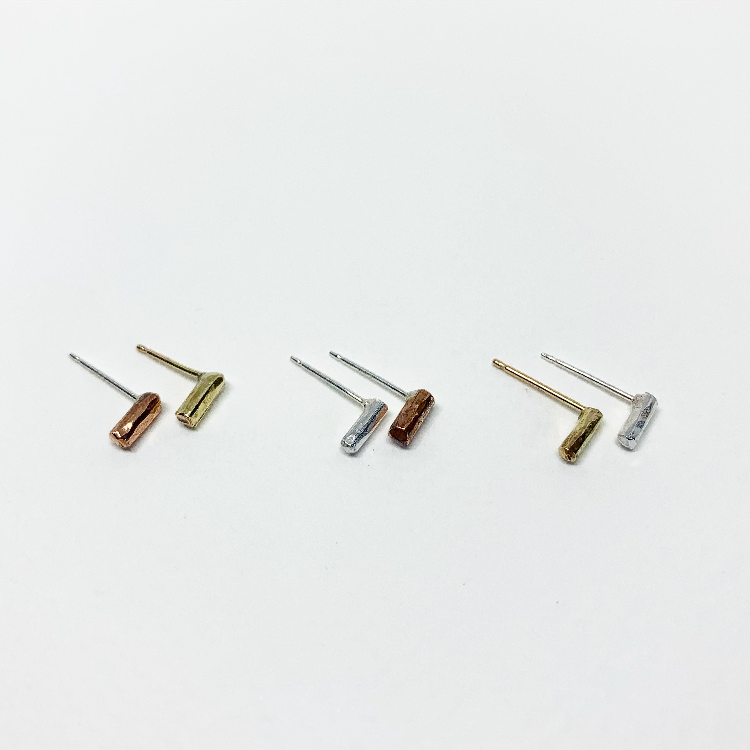 A pair of Mini Balance Stud Earrings - 1/4" featuring tiny hammered rods in copper, sterling silver, and yellow gold fill options, showcasing their minimalist design.