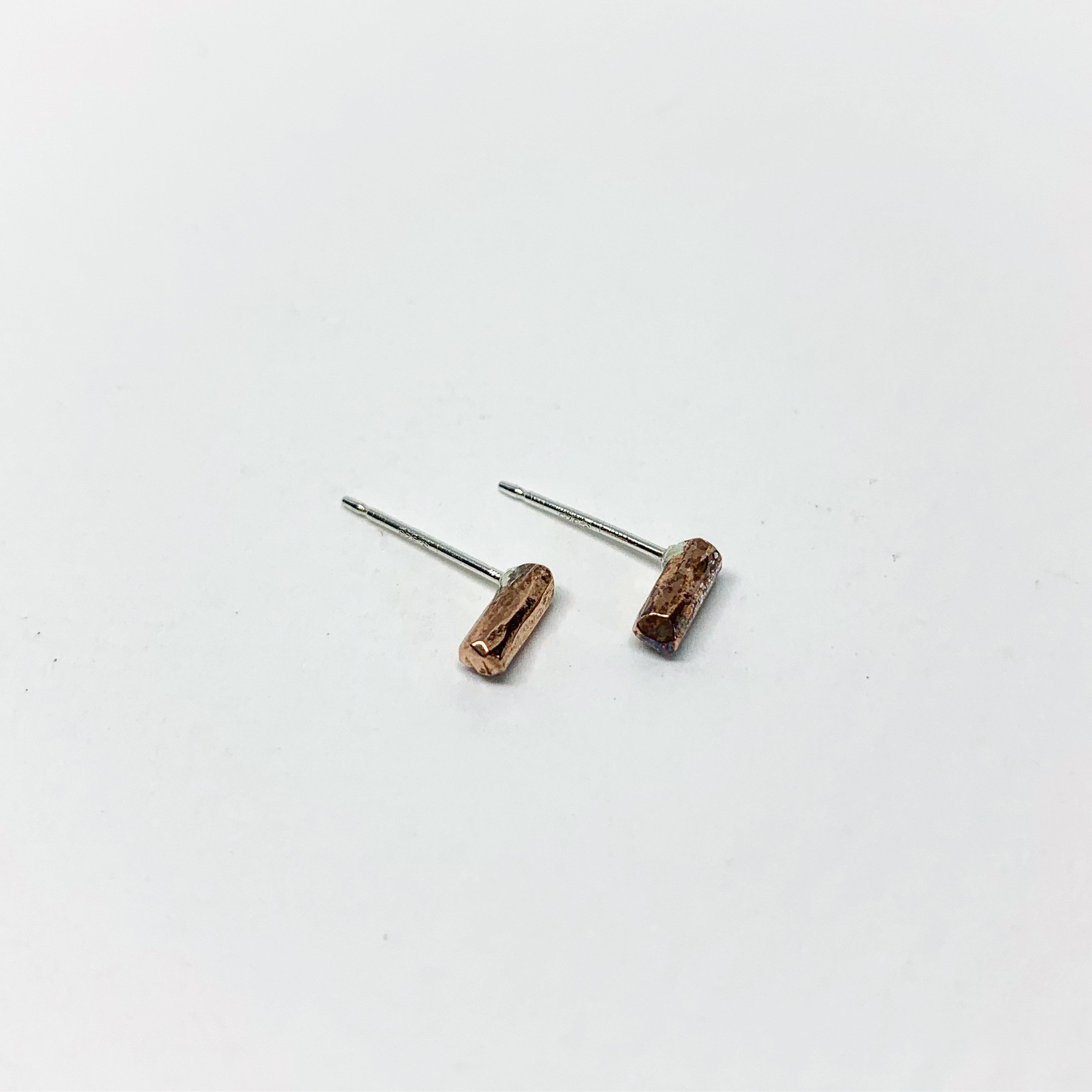 A pair of Mini Balance Stud Earrings - 1/4" featuring tiny hammered rods in copper, sterling silver, and yellow gold fill options, showcasing their minimalist design.