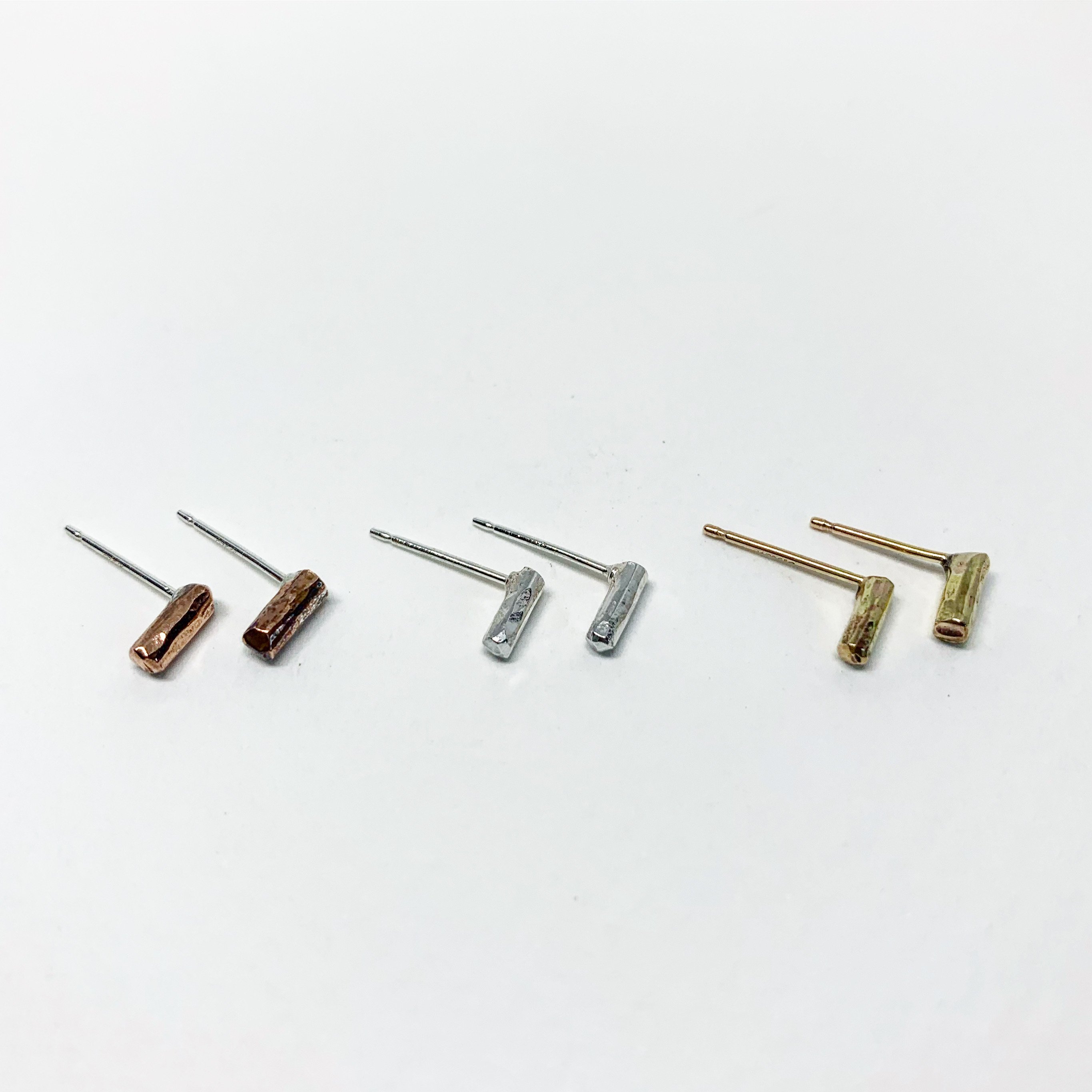 A pair of Mini Balance Stud Earrings - 1/4" featuring tiny hammered rods in copper, sterling silver, and yellow gold fill options, showcasing their minimalist design.