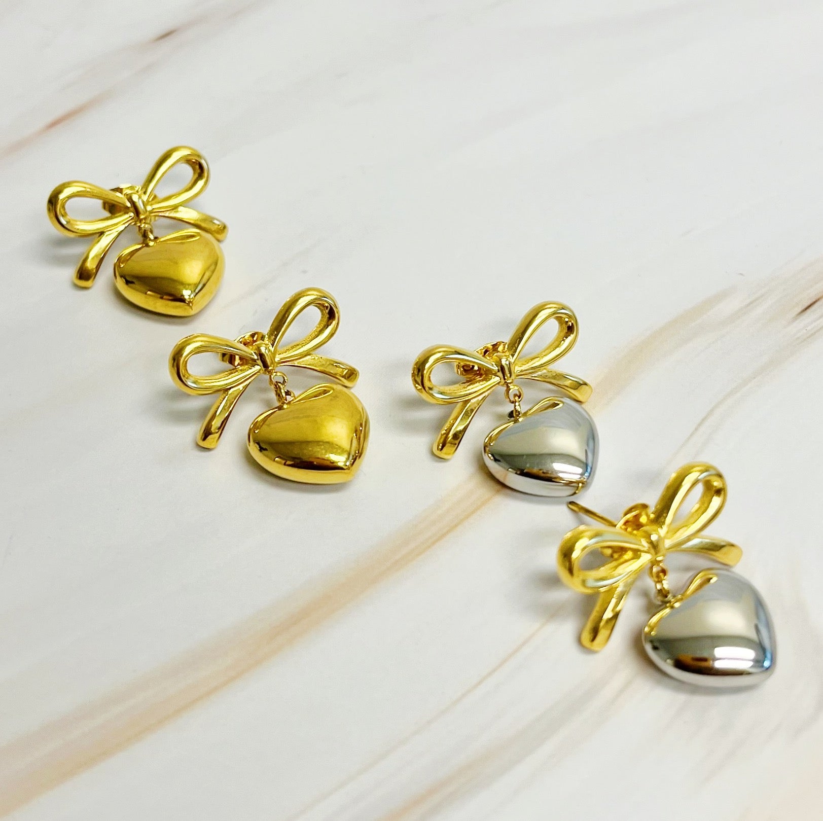 A pair of Mini Bow Mini Heart Earrings featuring a delicate bow and heart design, crafted from 18k gold plated stainless steel.