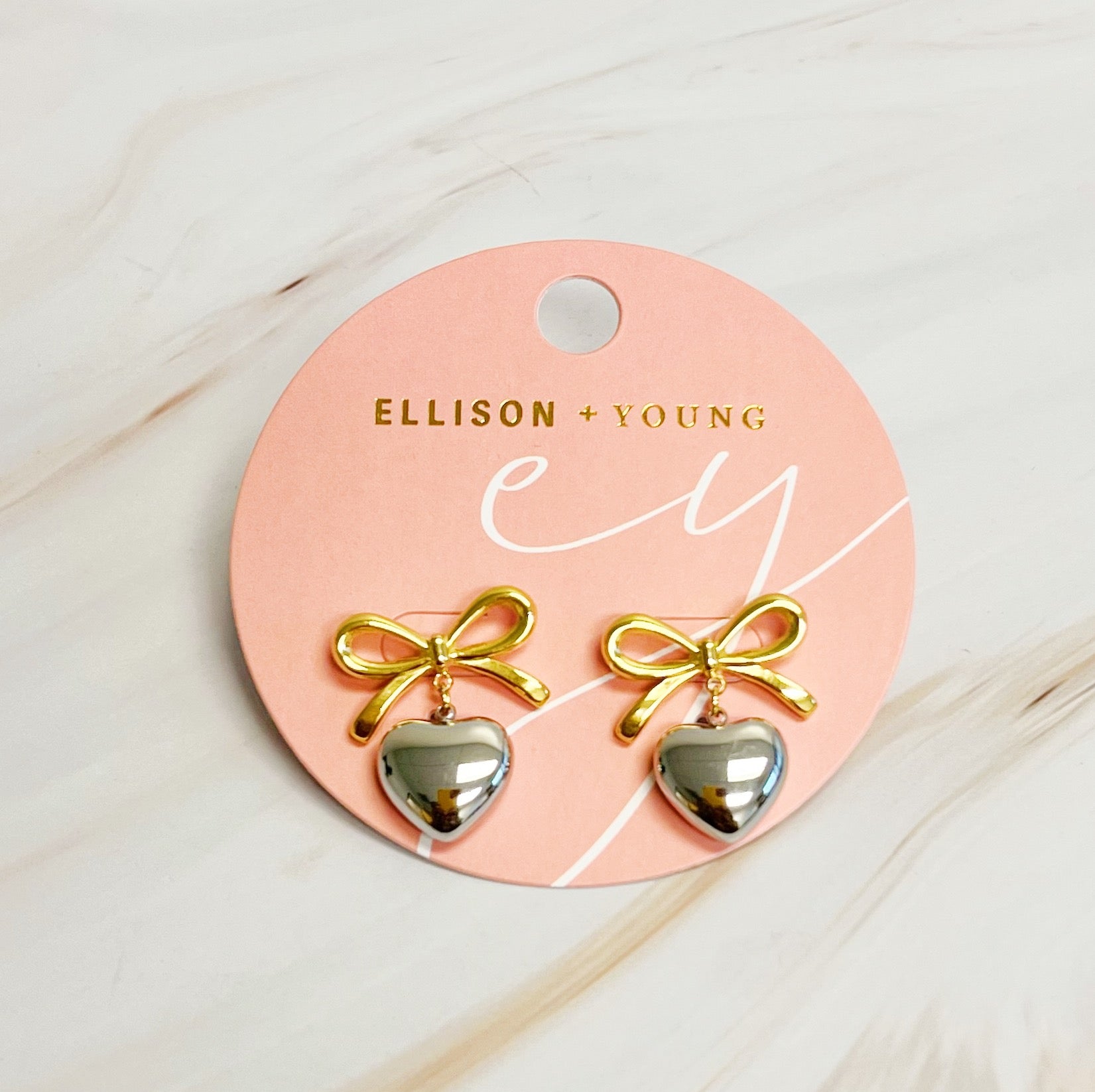 A pair of Mini Bow Mini Heart Earrings featuring a delicate bow and heart design, crafted from 18k gold plated stainless steel.