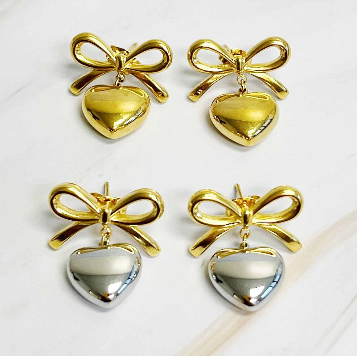 A pair of Mini Bow Mini Heart Earrings featuring a delicate bow and heart design, crafted from 18k gold plated stainless steel.