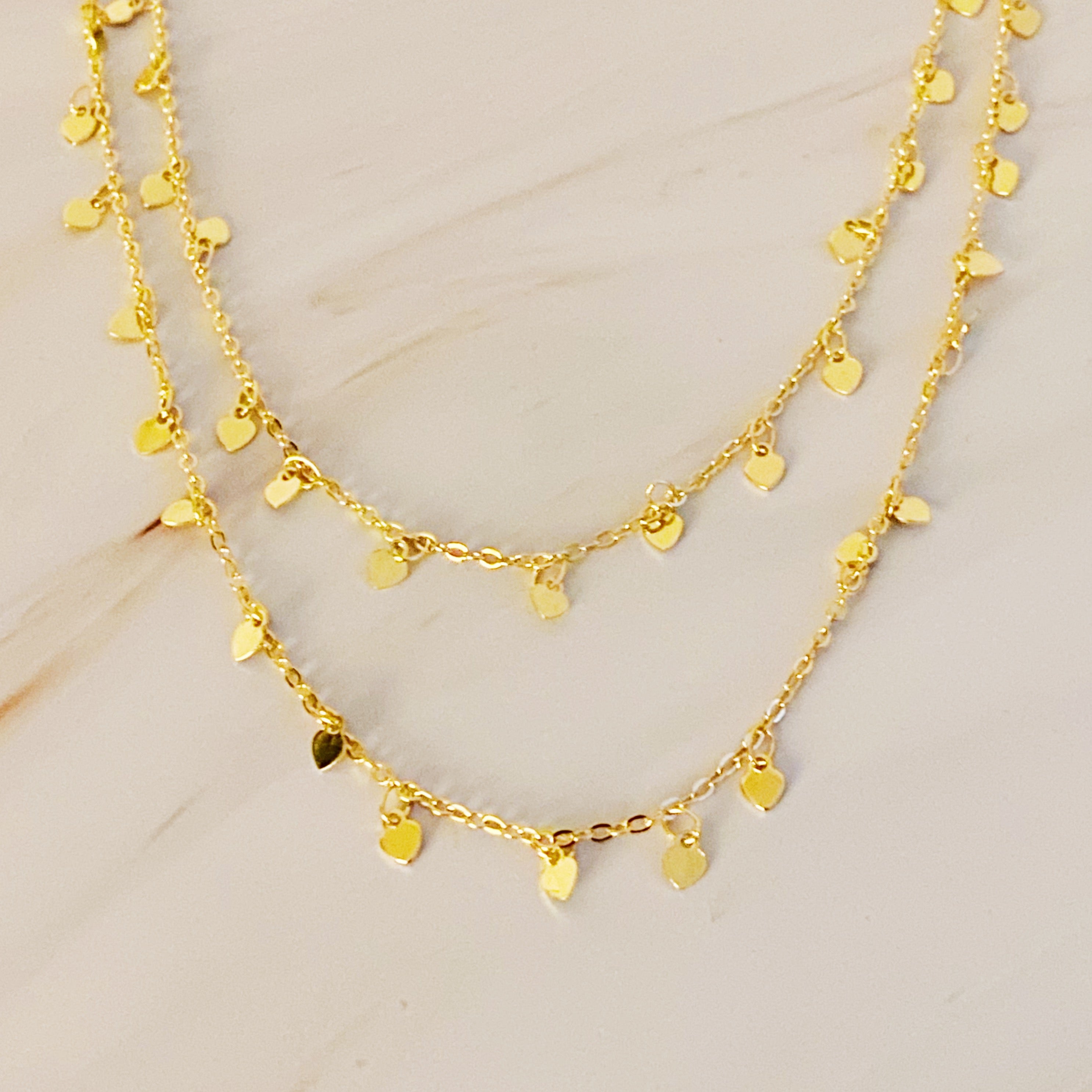 A long necklace featuring mini hearts on a gold chain, showcasing its elegant design and versatility.