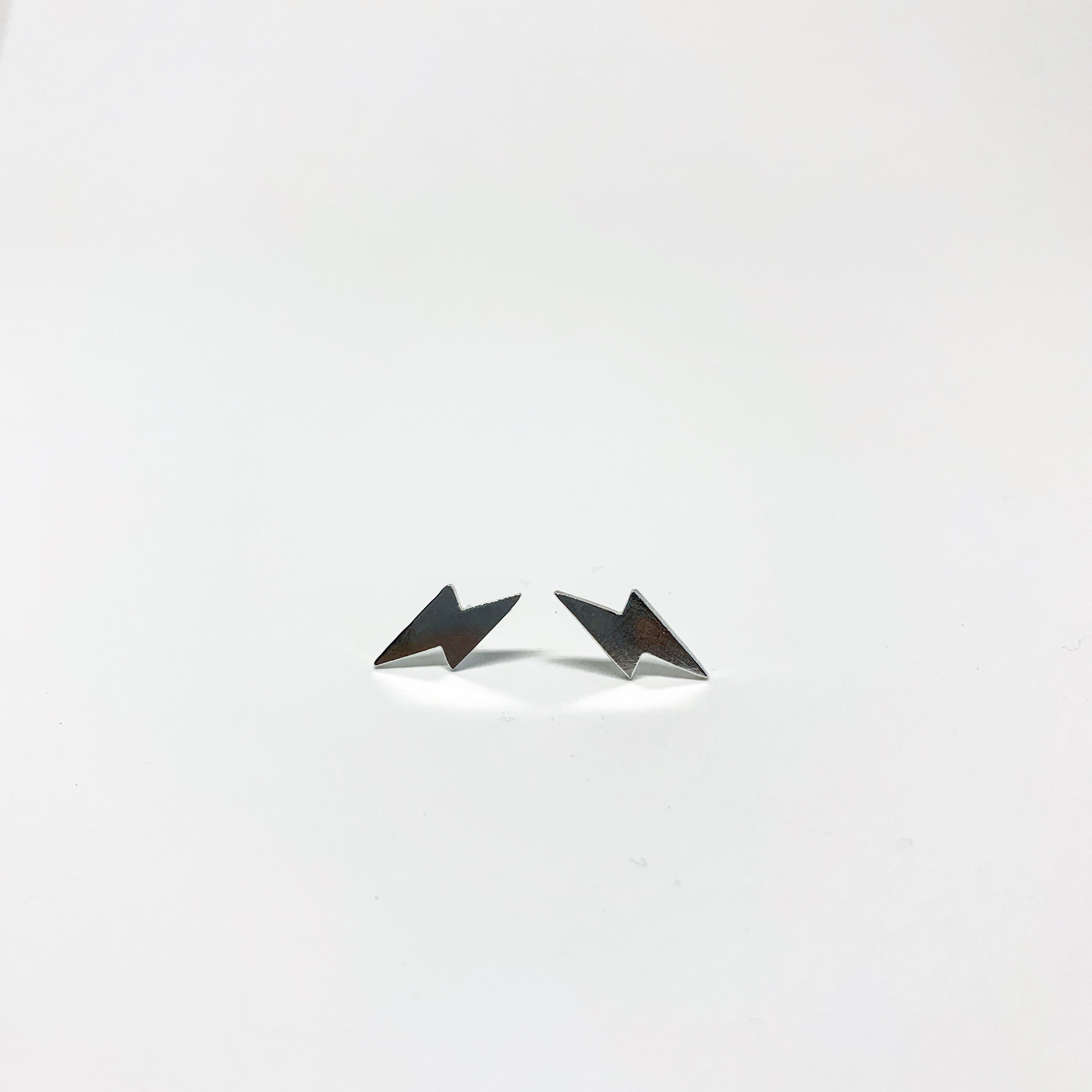 A pair of handmade mini lightning bolt stud earrings made from recycled sterling silver, showcasing a whimsical design.