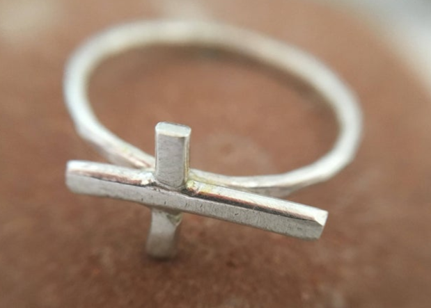 A delicate Mini Sideways Cross Ring made from recycled metals, featuring a hammered finish, symbolizing balance and humanity.