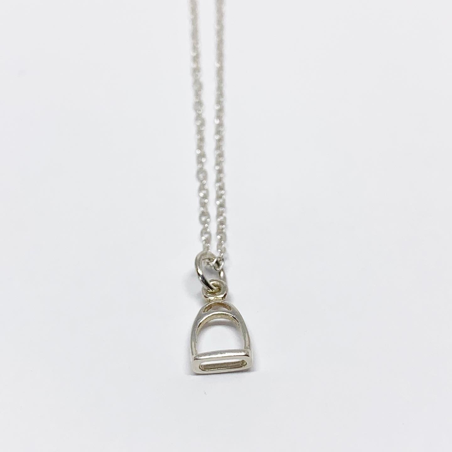 A delicate Mini Stirrup Charm Necklace featuring a sterling silver stirrup pendant, adjustable chain, and handmade craftsmanship.