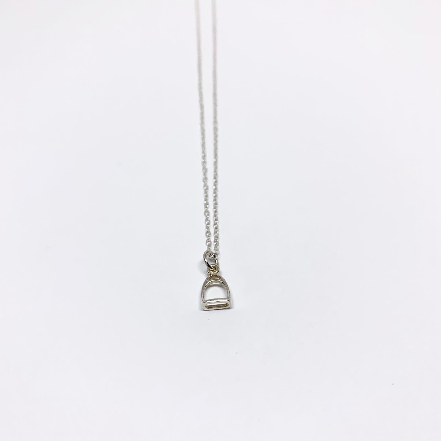 A delicate Mini Stirrup Charm Necklace featuring a sterling silver stirrup pendant, adjustable chain, and handmade craftsmanship.