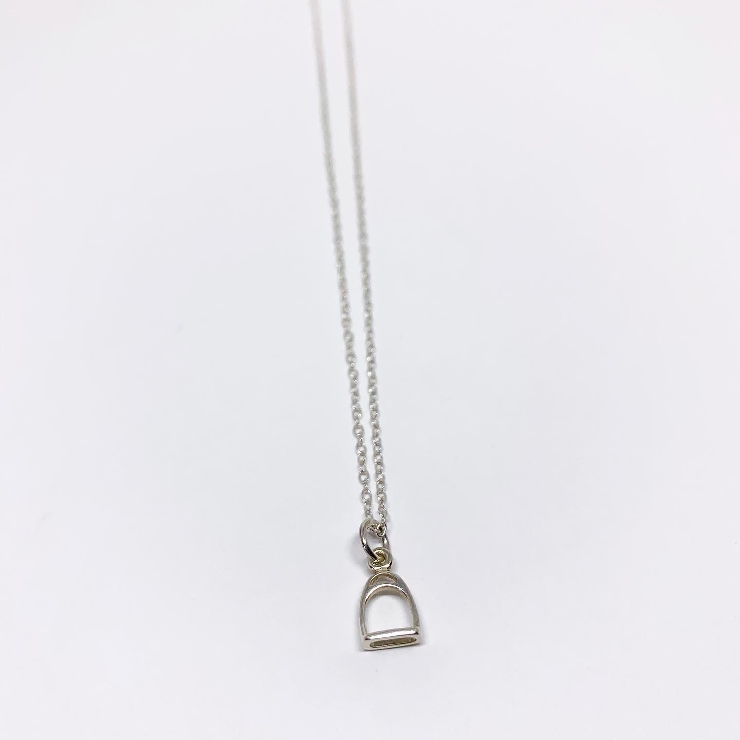 A delicate Mini Stirrup Charm Necklace featuring a sterling silver stirrup pendant, adjustable chain, and handmade craftsmanship.