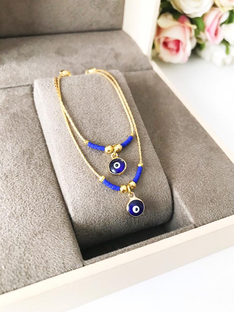 Minimal Evil Eye Bracelet featuring a blue glass charm and gold chain with tiny blue miyuki beads, elegantly designed for protection and style.