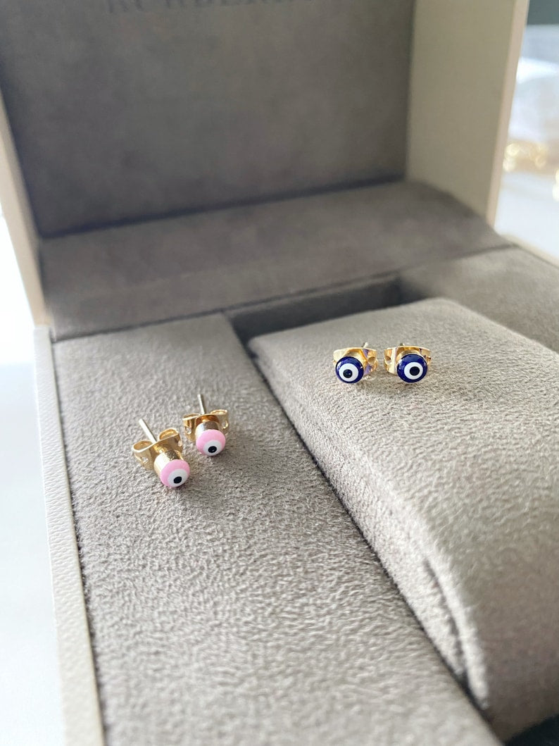 A pair of elegant gold minimal stud earrings featuring a tiny evil eye design in pink and blue options.