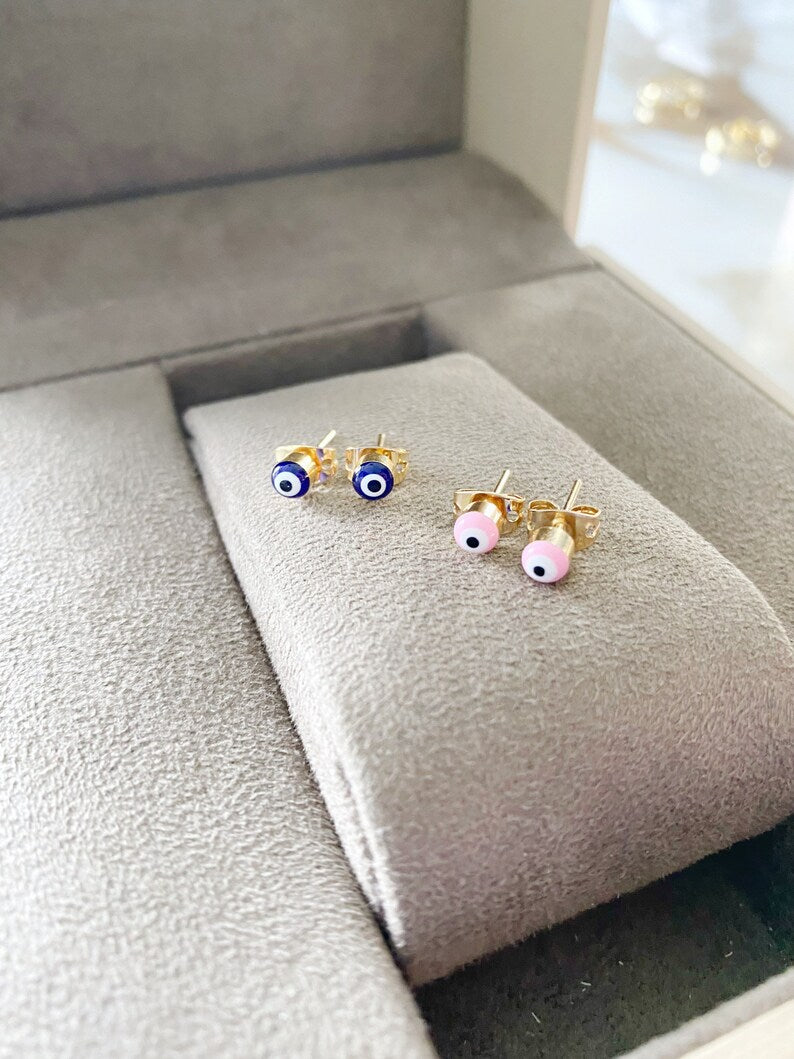 A pair of elegant gold minimal stud earrings featuring a tiny evil eye design in pink and blue options.