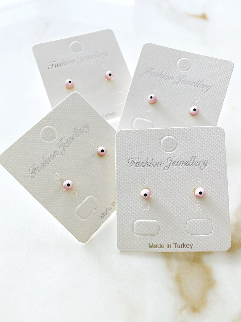 A pair of elegant gold minimal stud earrings featuring a tiny evil eye design in pink and blue options.