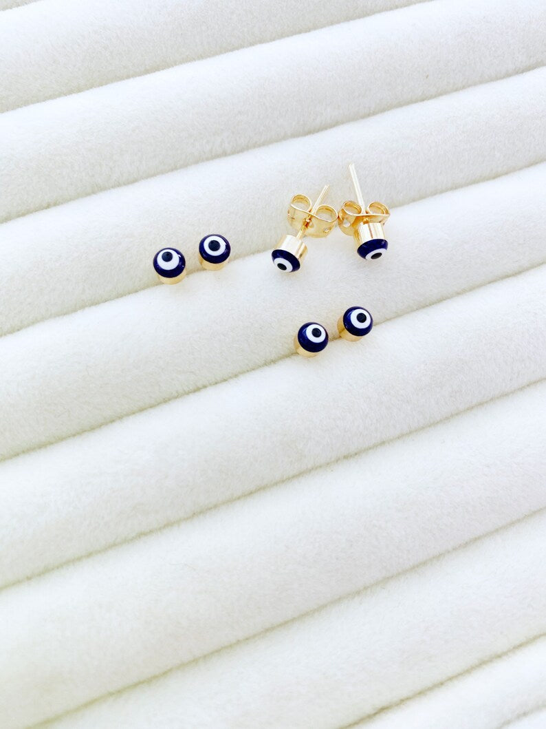 A pair of elegant gold minimal stud earrings featuring a tiny evil eye design in pink and blue options.