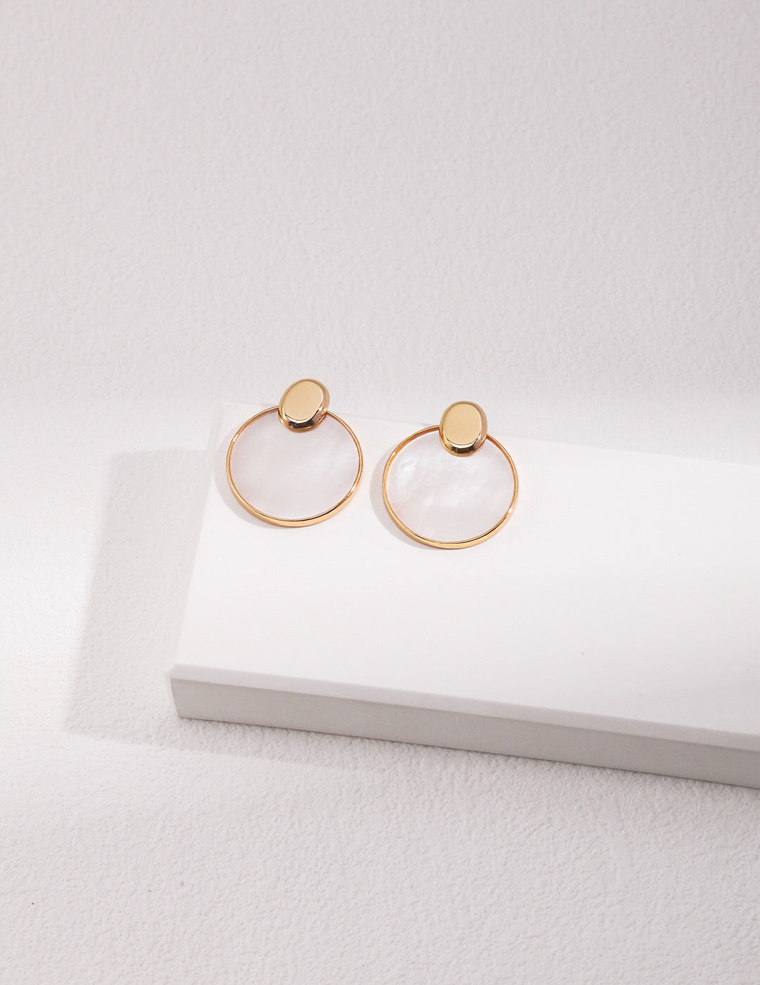 A pair of elegant Minimalist Detachable Mother-Of-Pearl Earrings featuring gold vermeil accents, displayed on a soft fabric background.