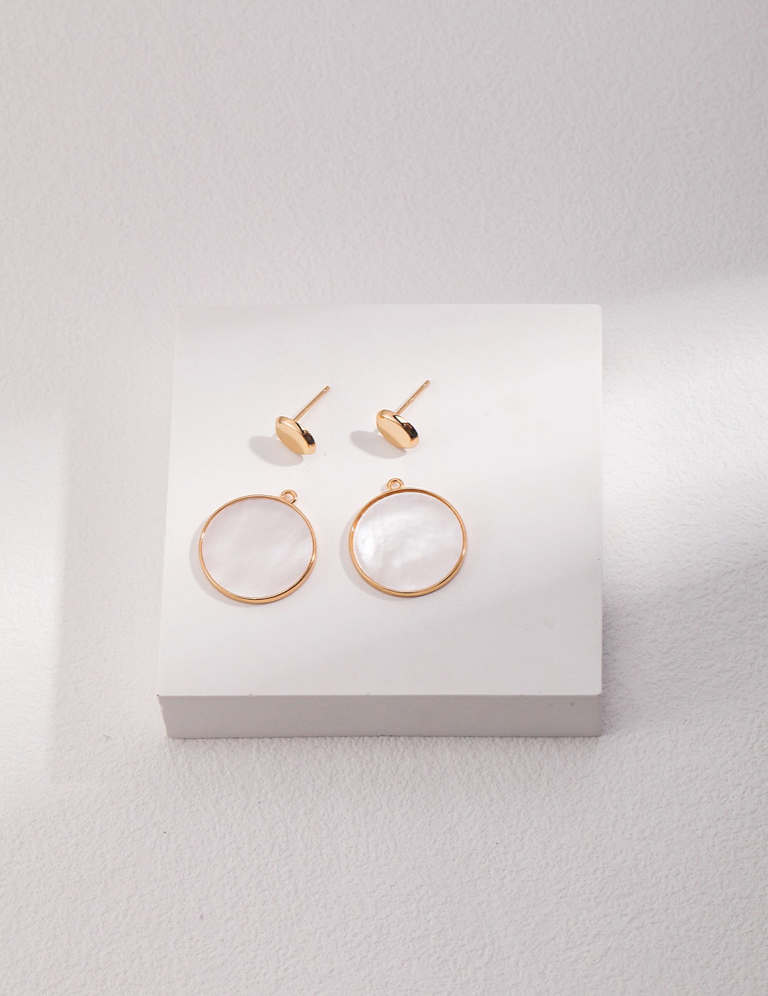 A pair of elegant Minimalist Detachable Mother-Of-Pearl Earrings featuring gold vermeil accents, displayed on a soft fabric background.